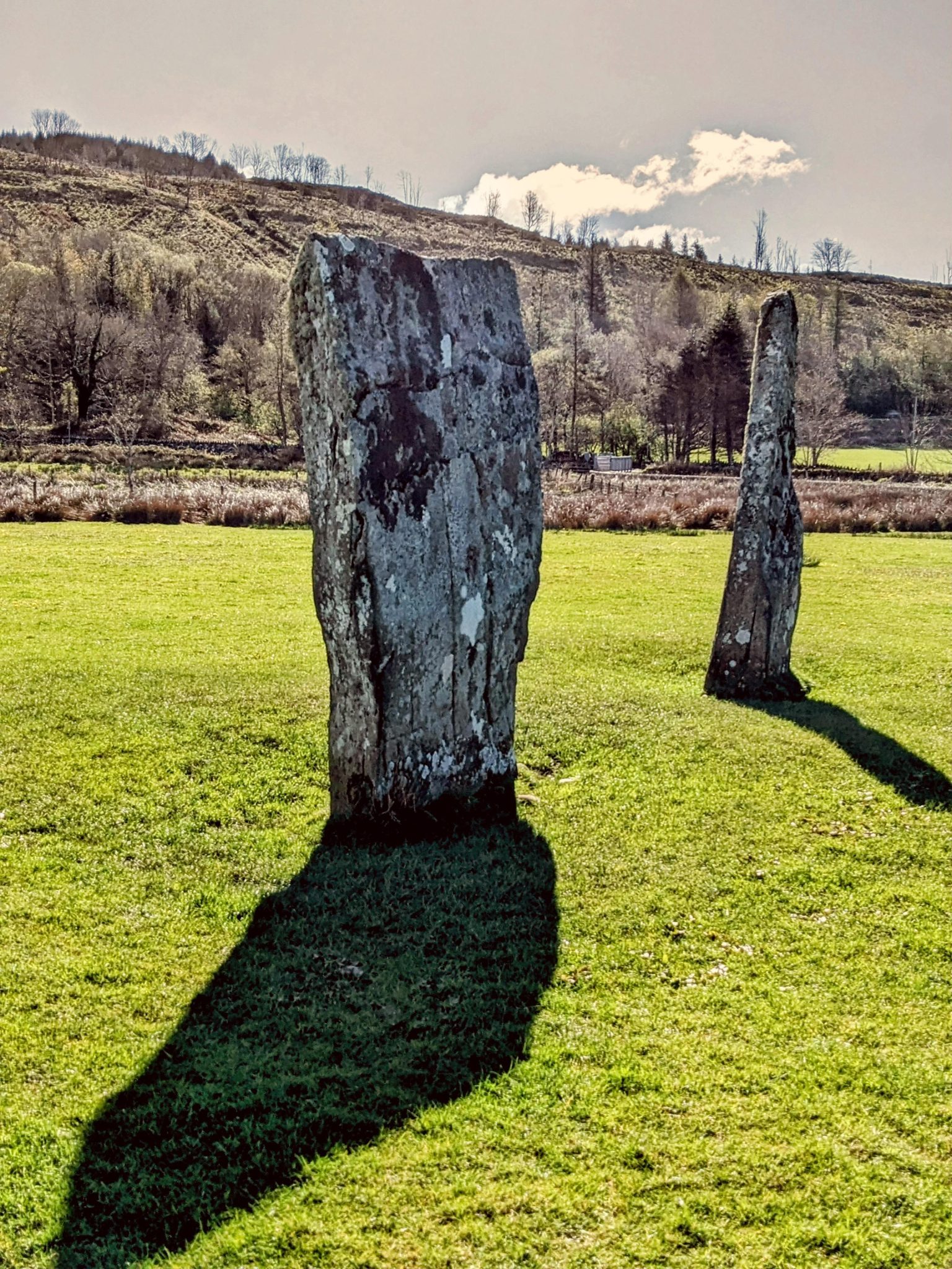 Two tall standing stones in a green field at Nether Largie, Kilmartin Glen, with hills behind.