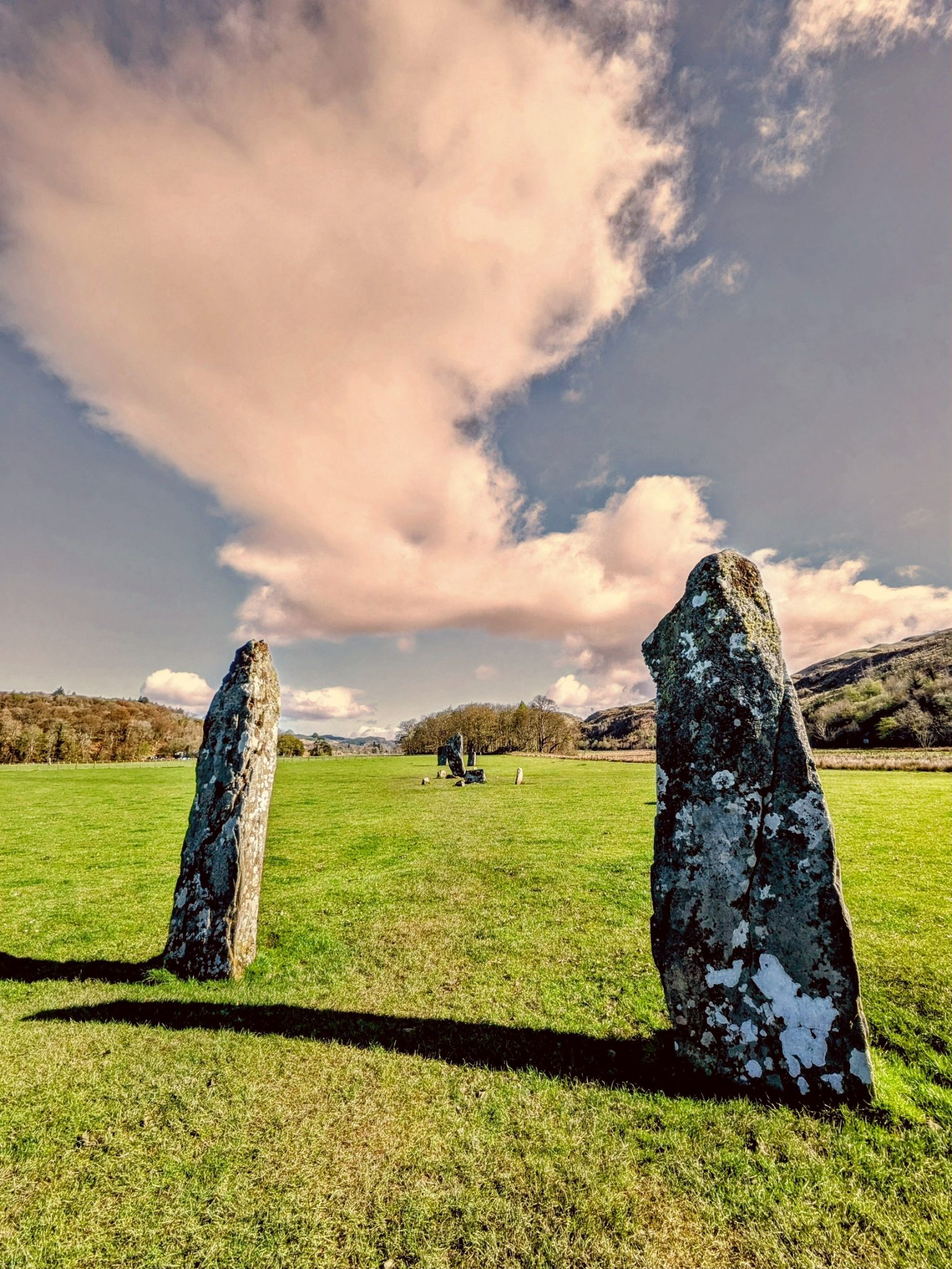 A single tall lichen-covered standing stone rising from a green field at Kilmartin Glen.