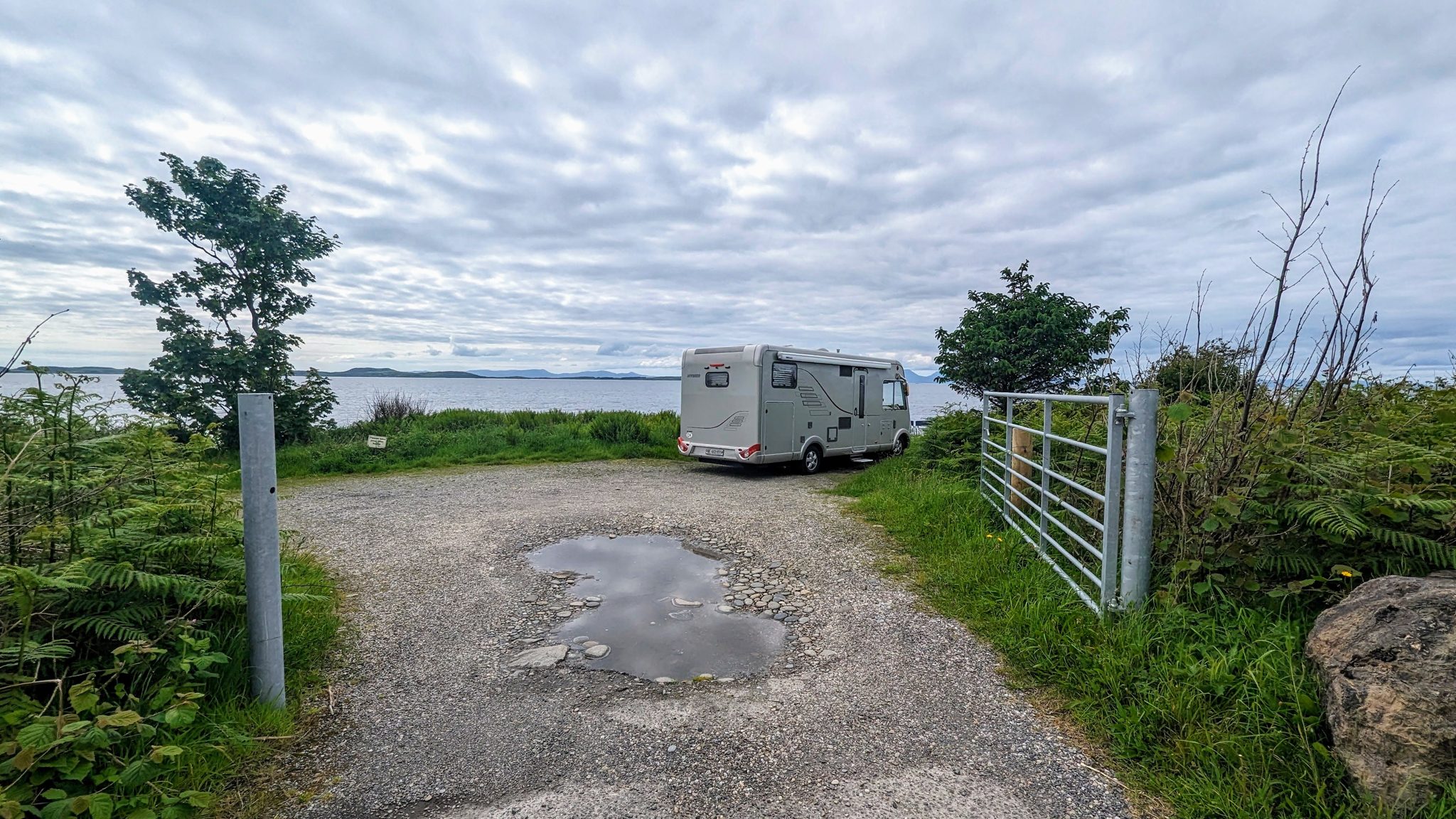 A Hymer motorhome parked on a gravel area above the shore on the east Kintyre coast, gate and sea beyond.