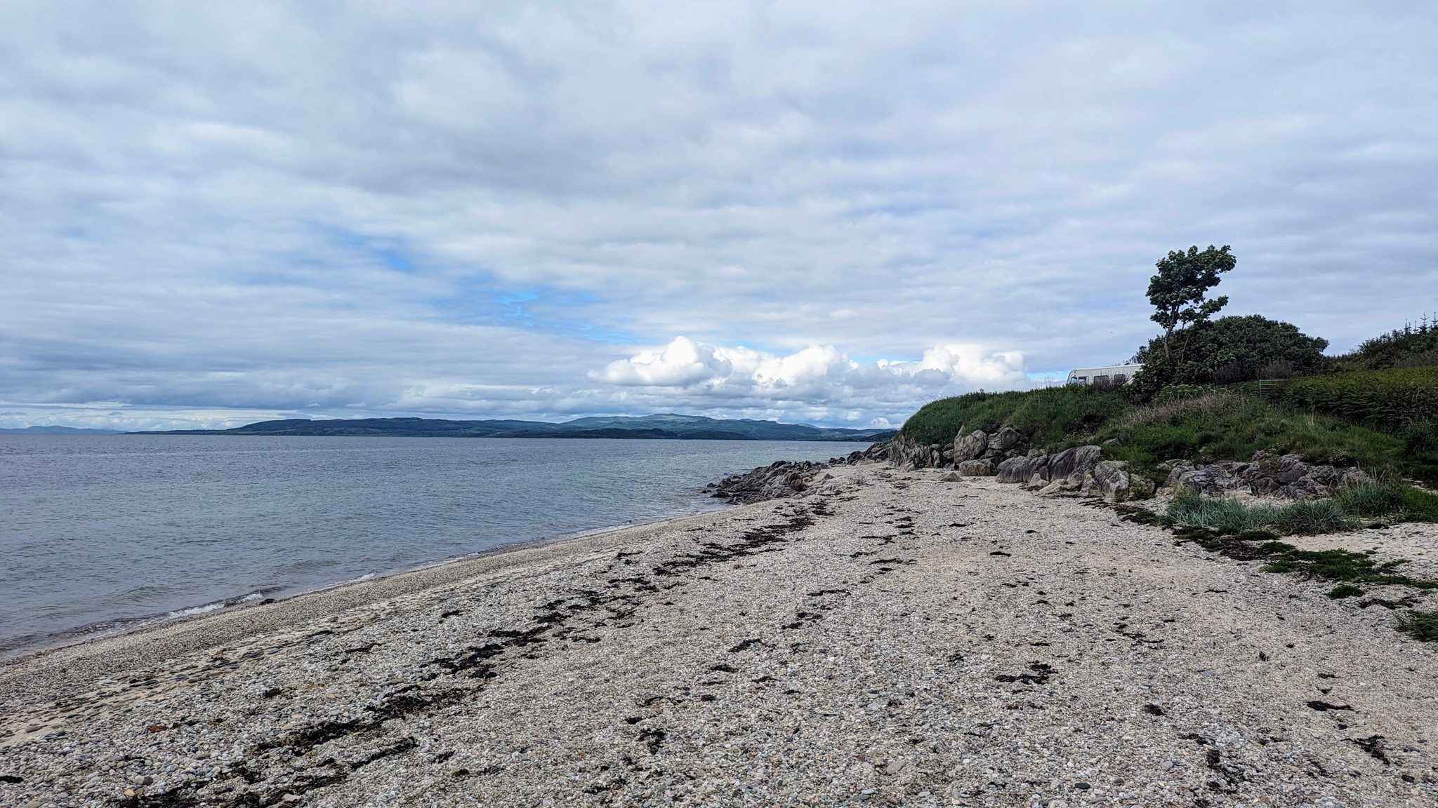 The pebble beach curving to a rocky point on the east Kintyre coast, Arran across the water.