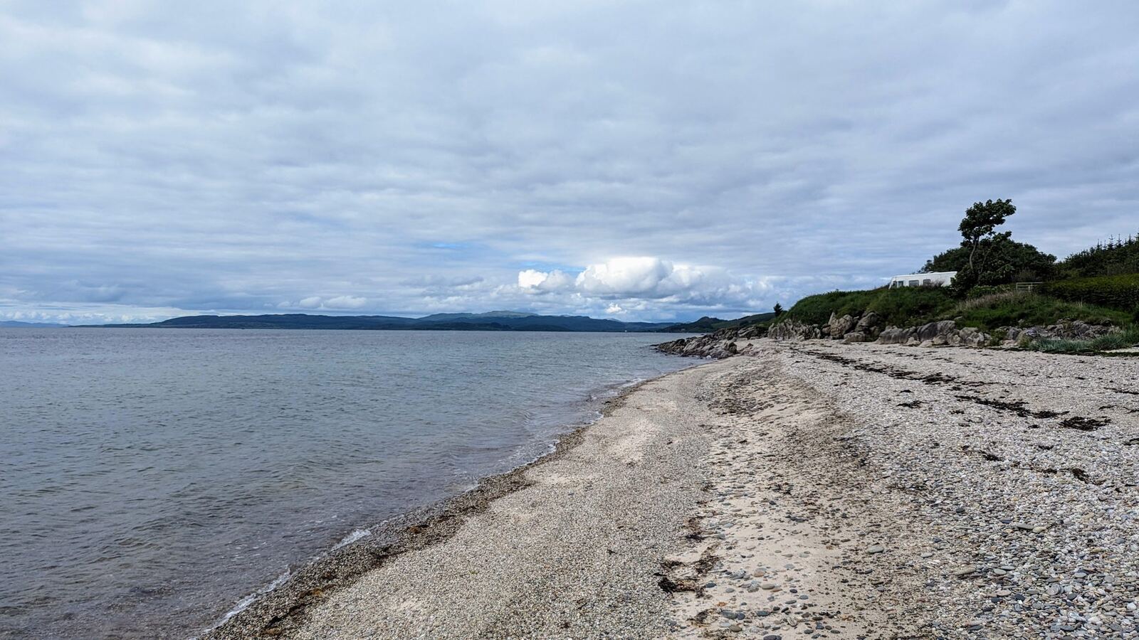 A shingle beach on the east Kintyre coast leading to the sea, an island on the horizon.