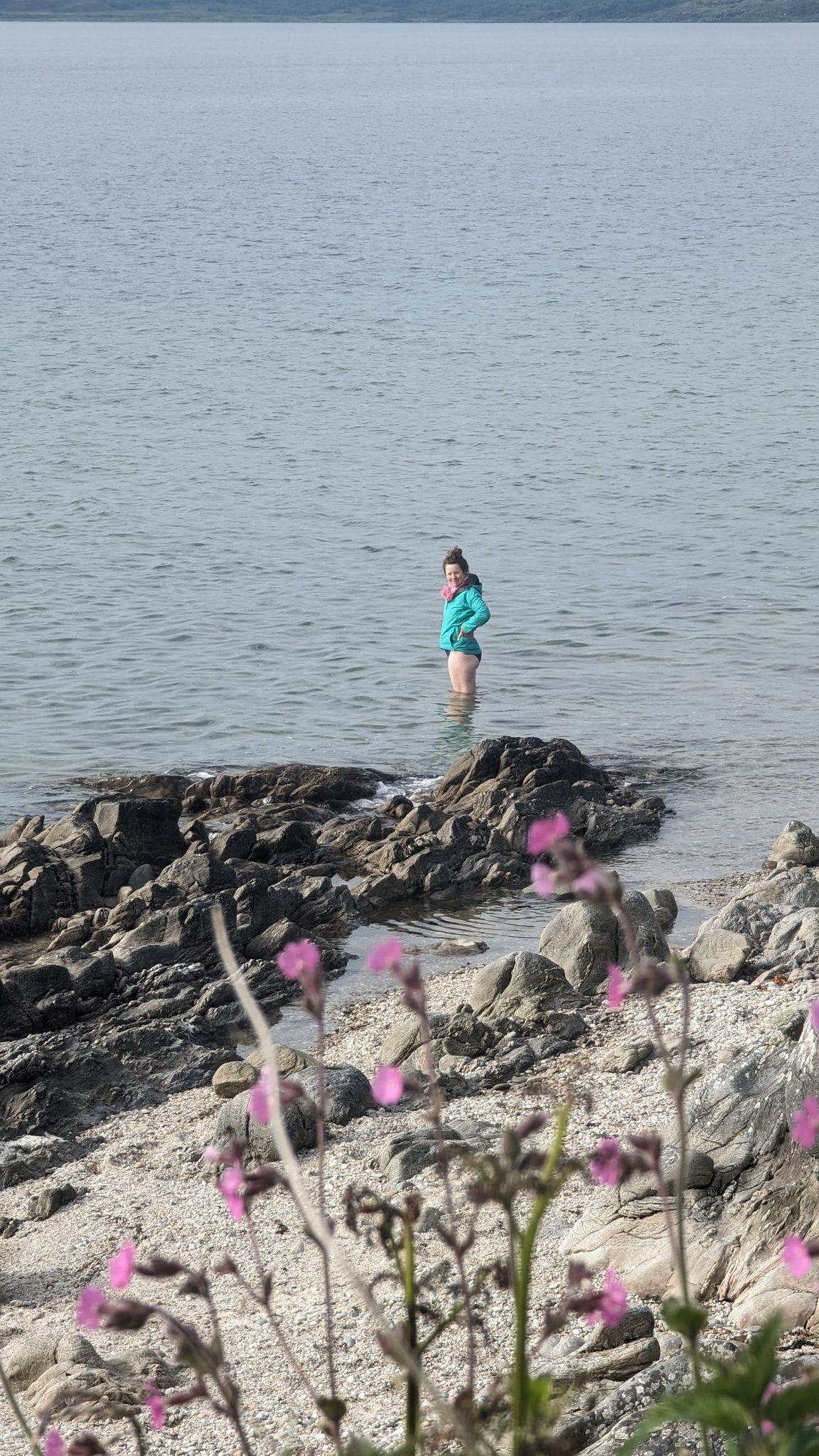 A woman paddling in the clear shallow sea off the rocks on the east Kintyre shore.