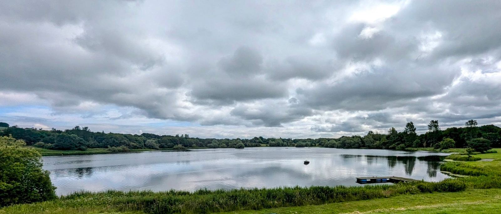 Still evening light on Linlithgow Loch with soft reflections and reed beds in the foreground.
