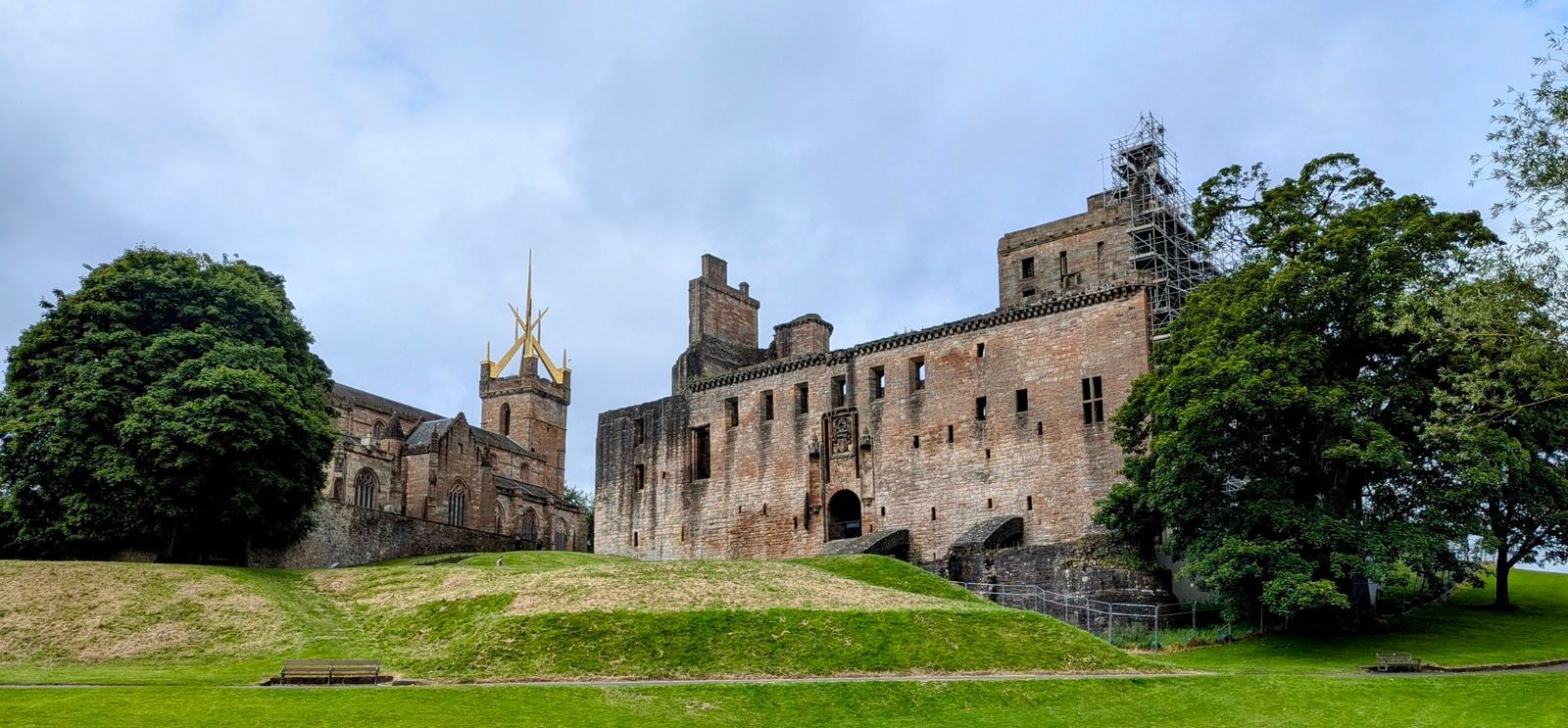 The tall stone gatehouse and entrance front of Linlithgow Palace rising above the green, under a moody sky.