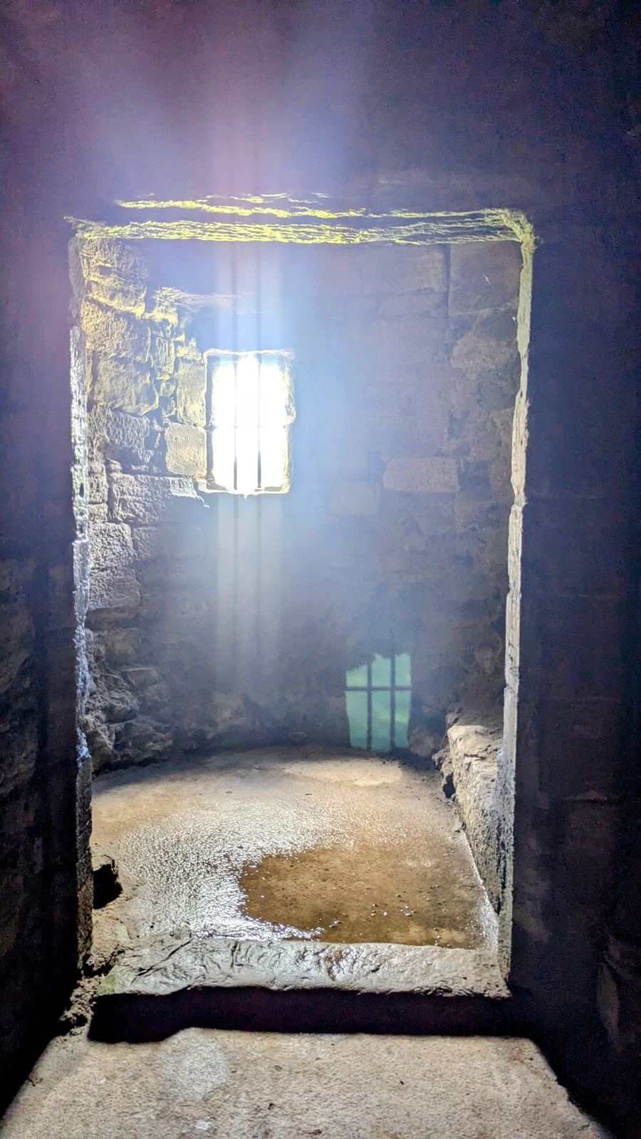 A shaft of daylight falling through a tall window into a dim stone chamber of Linlithgow Palace.