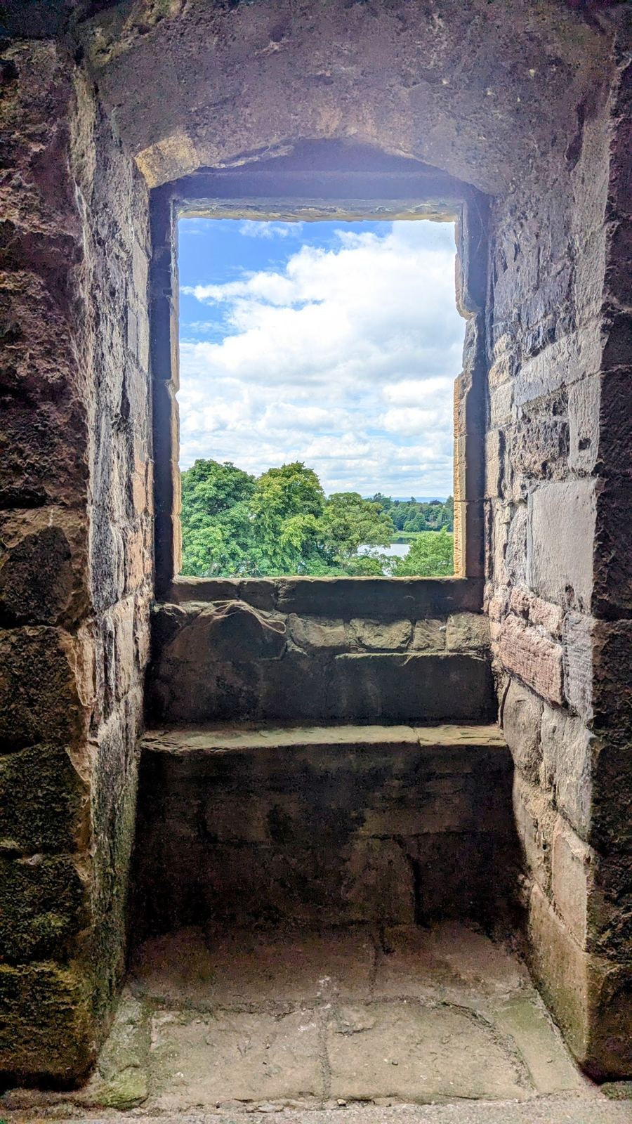 The calm loch and far shore framed in a tall stone window of Linlithgow Palace.