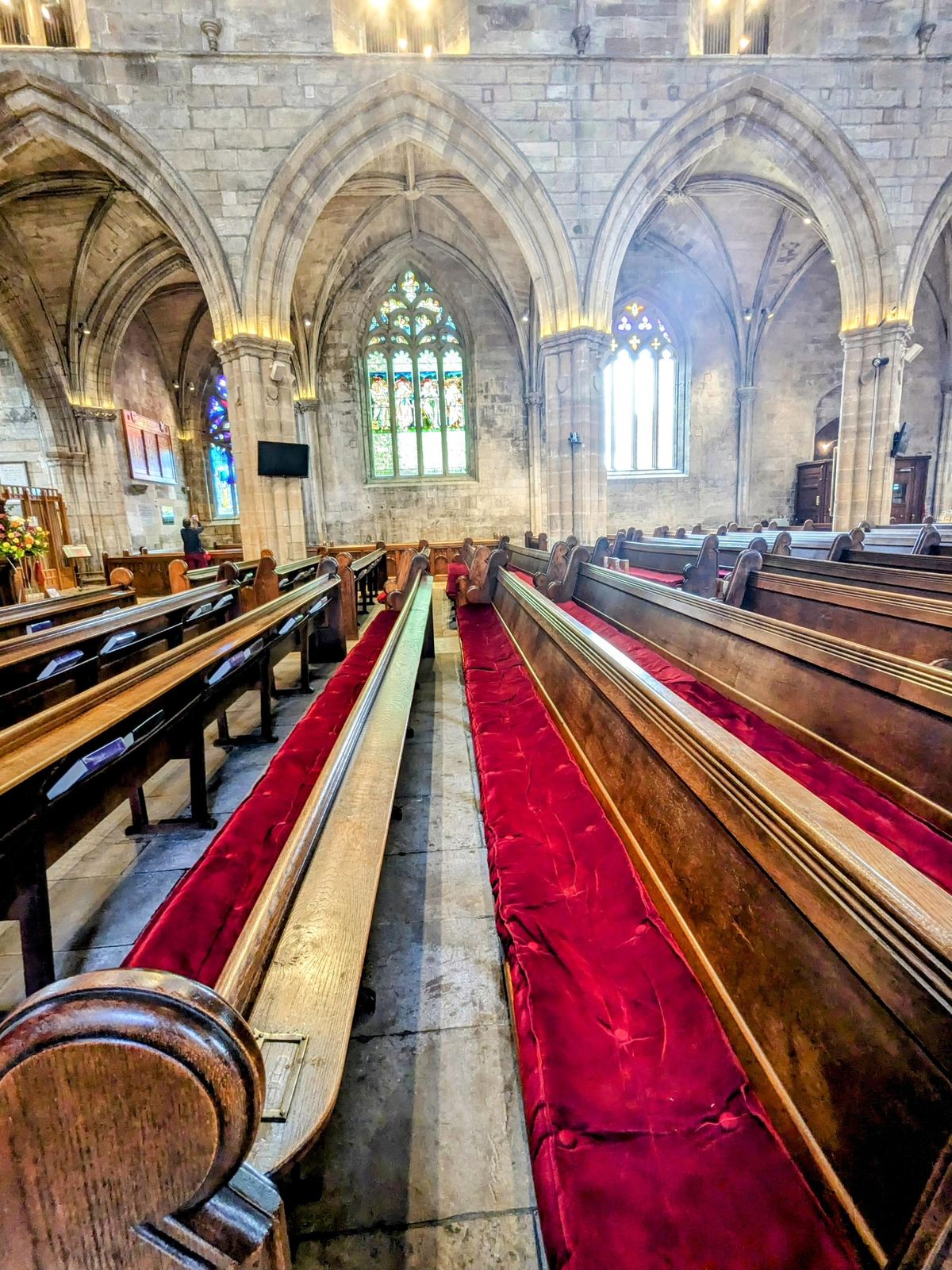 The long Gothic nave of St Michael's Church, Linlithgow, with wooden pews, a red carpet runner and tall arched windows.