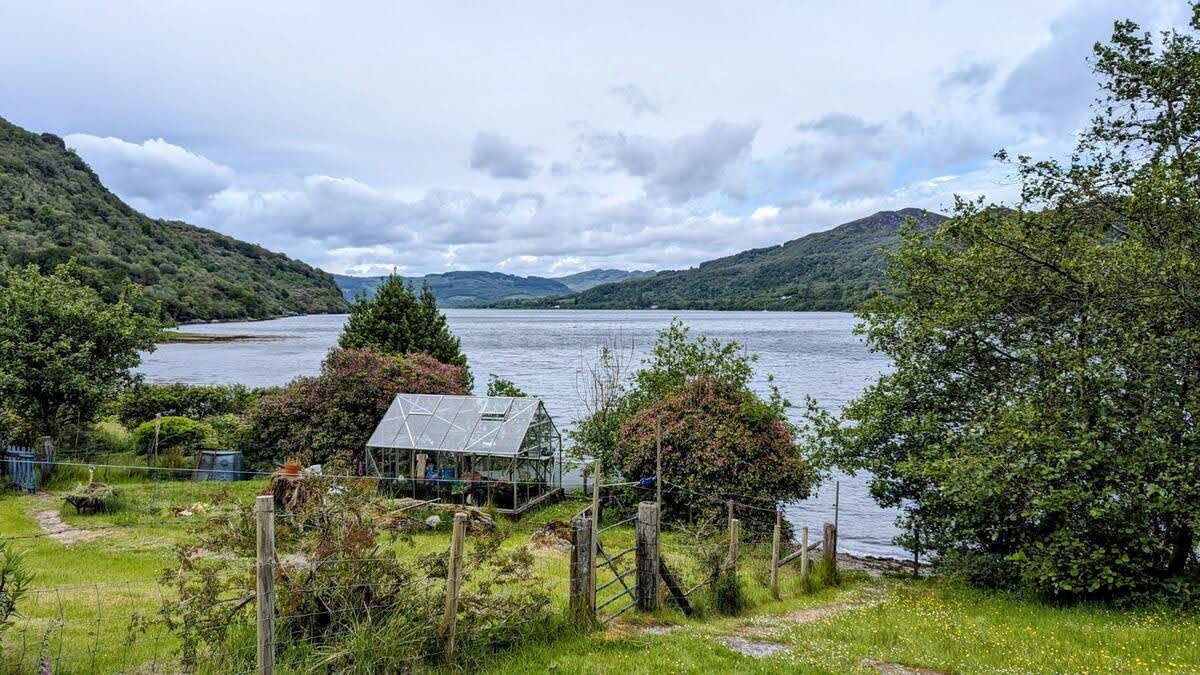 A cottage on the wooded shore of Loch Riddon, the calm loch beyond.