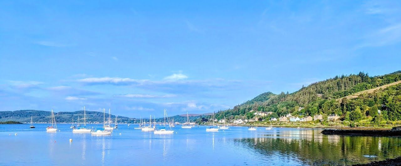 Yachts moored on the calm Kyles of Bute off Tighnabruaich at the mouth of Loch Riddon, reflected in the water.