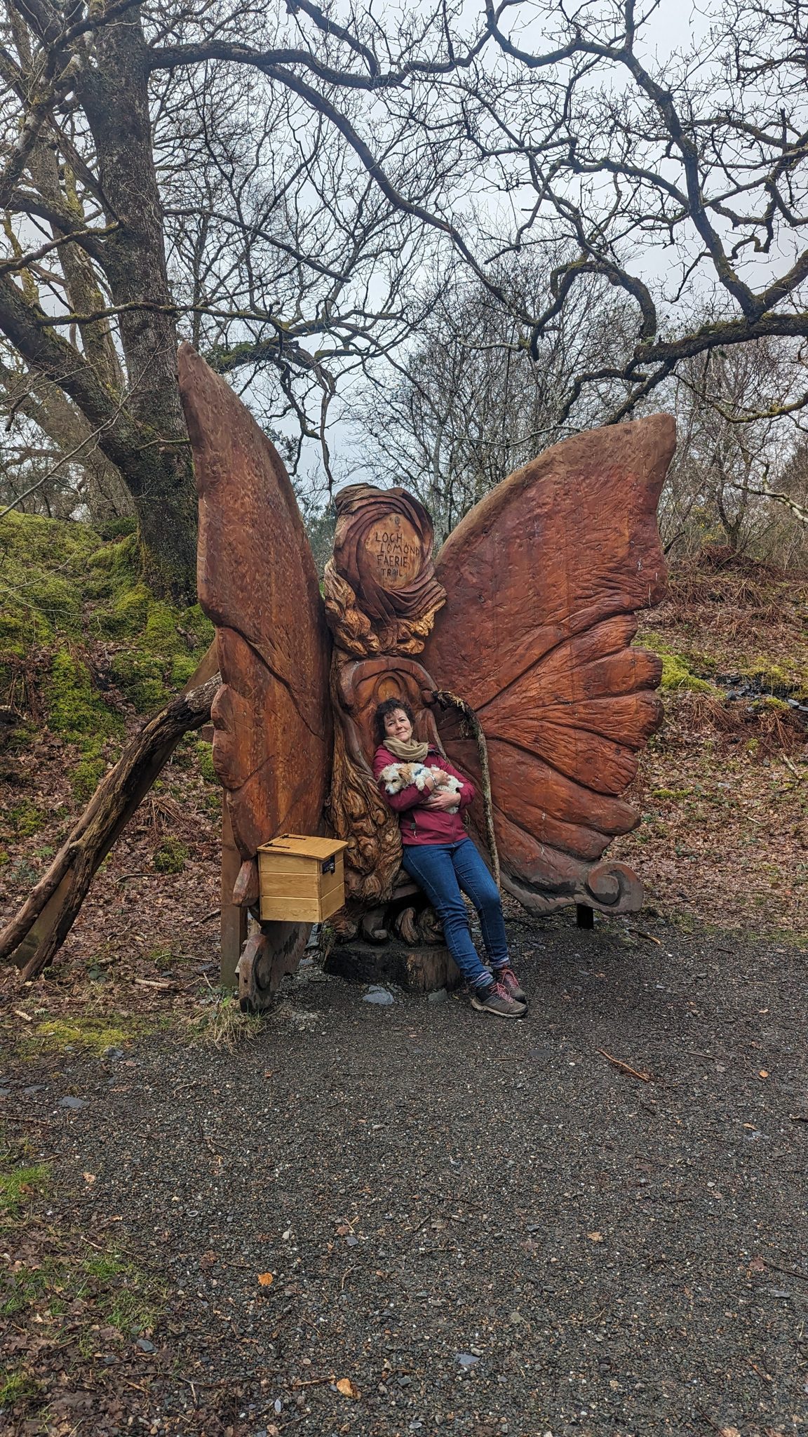 A person sitting in a huge carved wooden throne with butterfly wings on the Loch Lomond fairy trail at Luss.