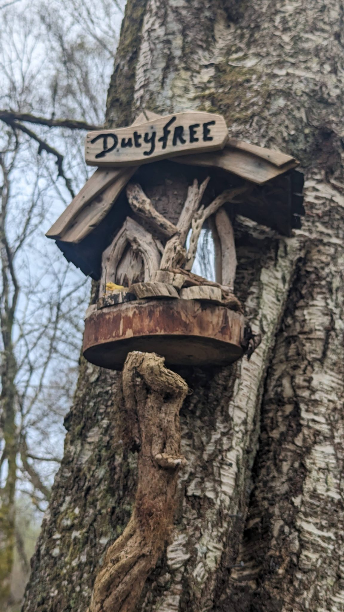 A carved wooden fairy house on a tree labelled 'Duty Free' on the Luss fairy trail.