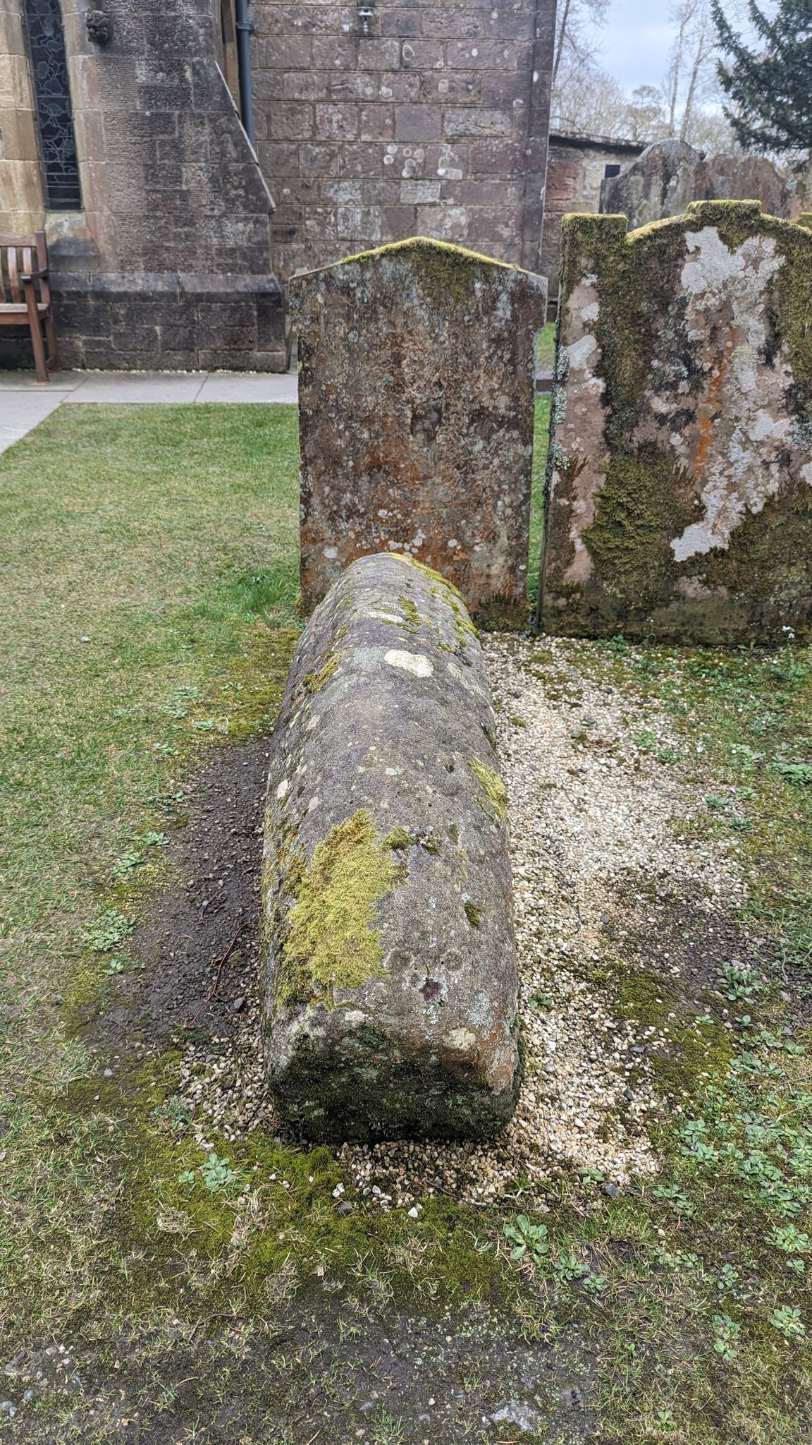 A weathered recumbent carved effigy stone in the churchyard at Luss.
