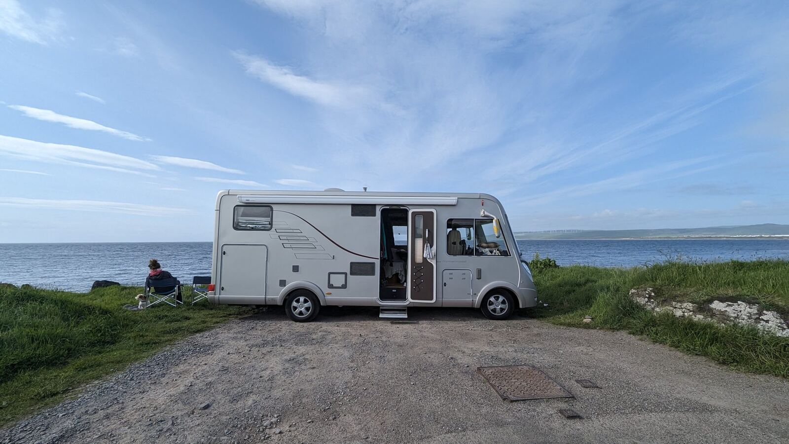 A motorhome parked by the shore at Machrihanish in the evening, a person sitting on a chair looking out over the Atlantic.