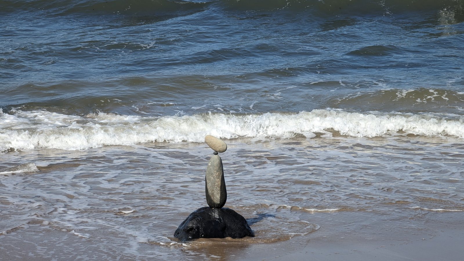 A balanced-stone cairn on a rock with the surf washing in, North Berwick beach.
