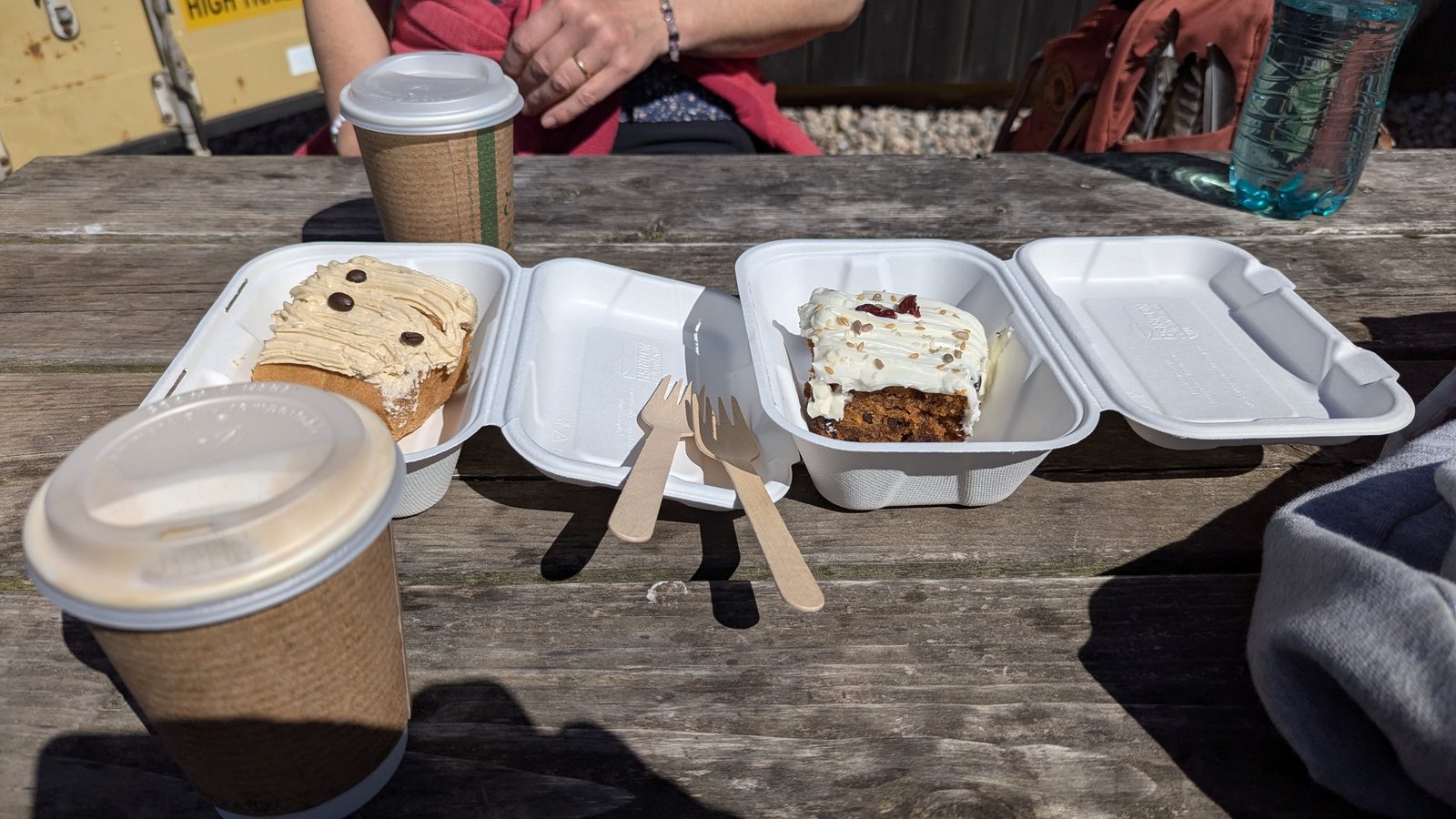 Two slabs of cake — coffee and walnut, and carrot cake — with takeaway coffees on a picnic bench outside Drift café at Canty Bay, North Berwick.