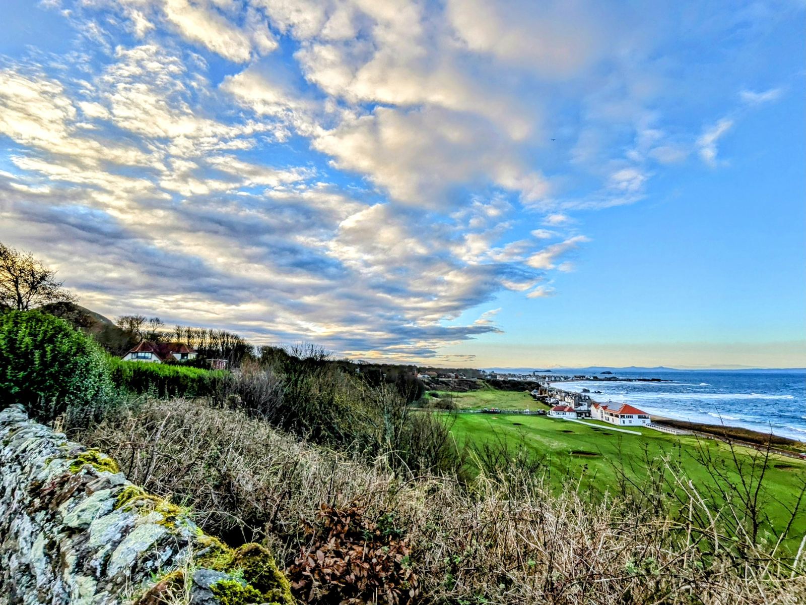 Clifftop links golf course greens running along the grassy coast at North Berwick with the sea and a big sky beyond.