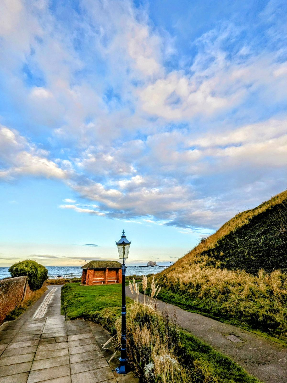 A grassy coastal path with a couple of benches leading toward North Berwick Law under a big blue sky.