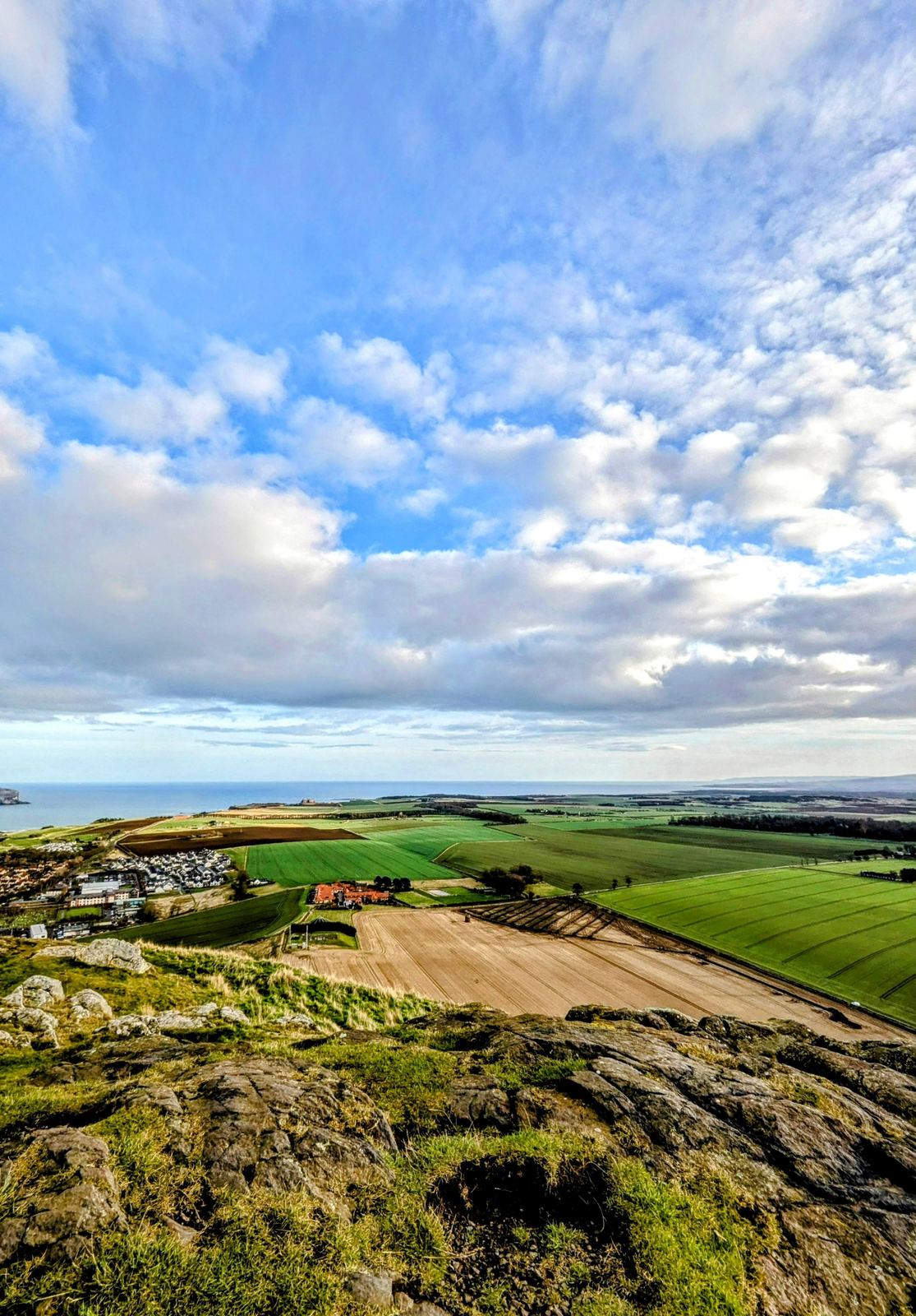 Green farm fields meeting the East Lothian coastline near North Berwick under a wide, bright sky.