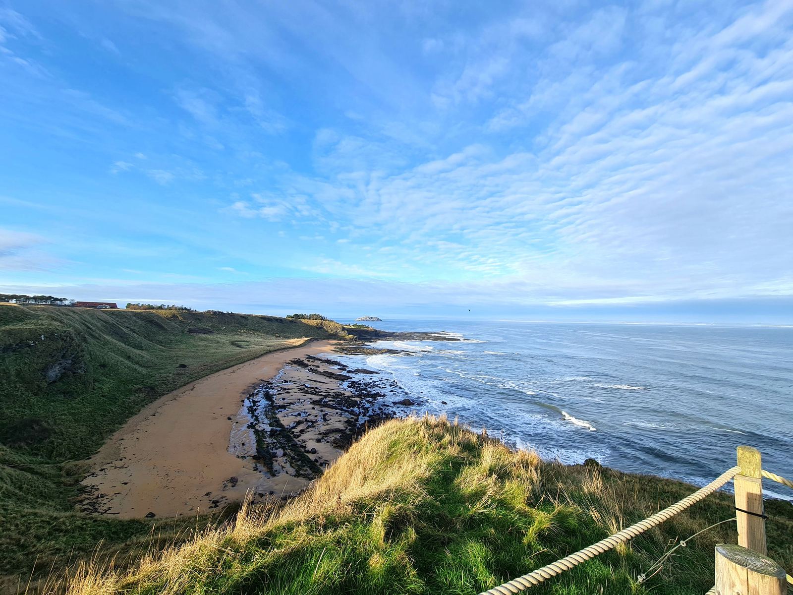 North Berwick Law, the conical volcanic hill, rising beyond a grassy coastal path and the sea near North Berwick.