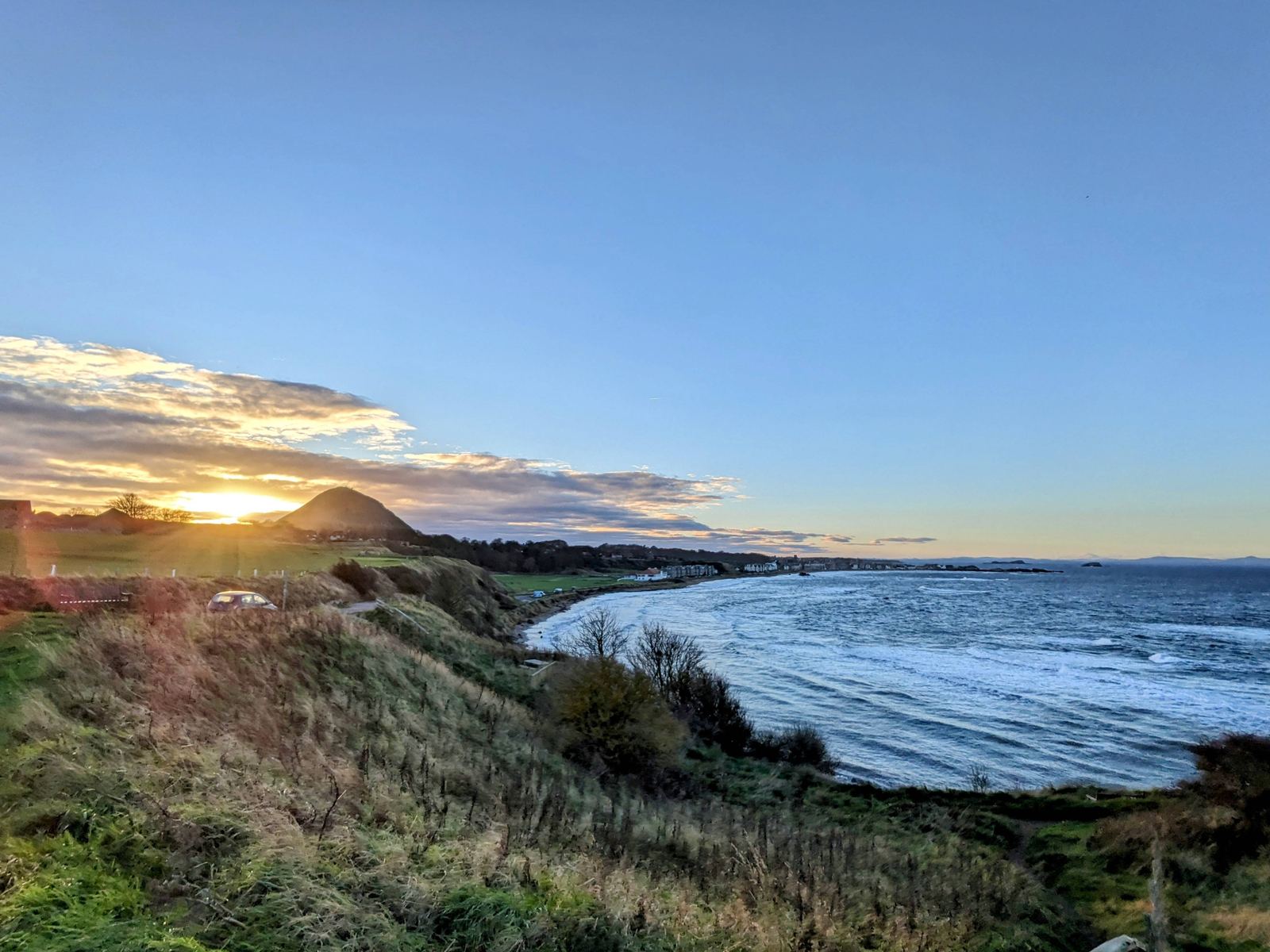 A low sun setting over the sea and coastline at North Berwick, the sky glowing orange behind a headland.