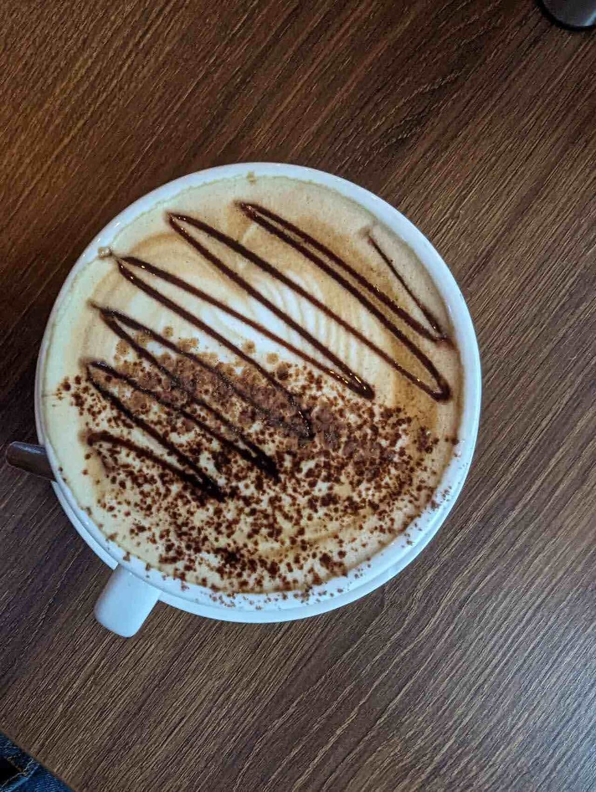 A large mug of hot chocolate topped with chocolate drizzle on a wooden café table.