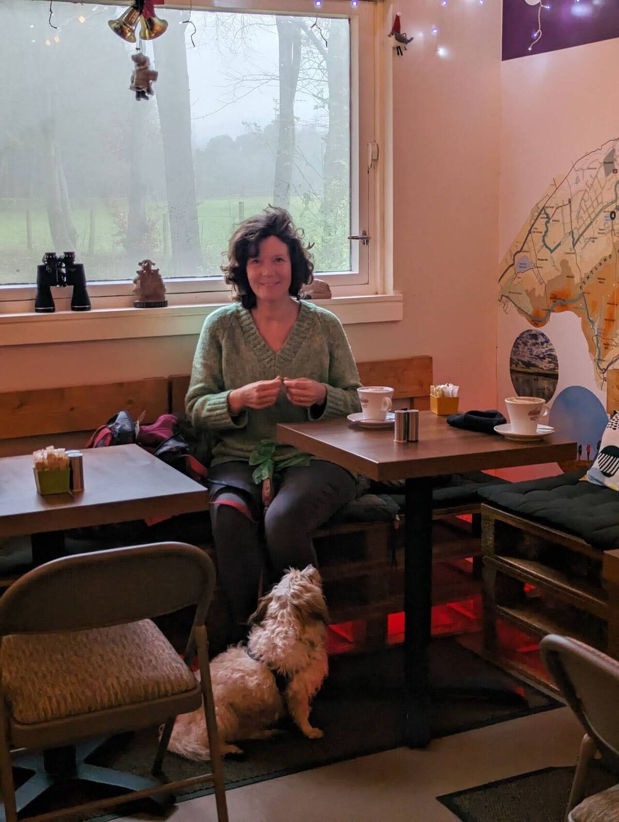 Inside the cosy Flotterstone café, a couple and a small dog at a table under a Welcome to the Pentlands banner and fairy lights.