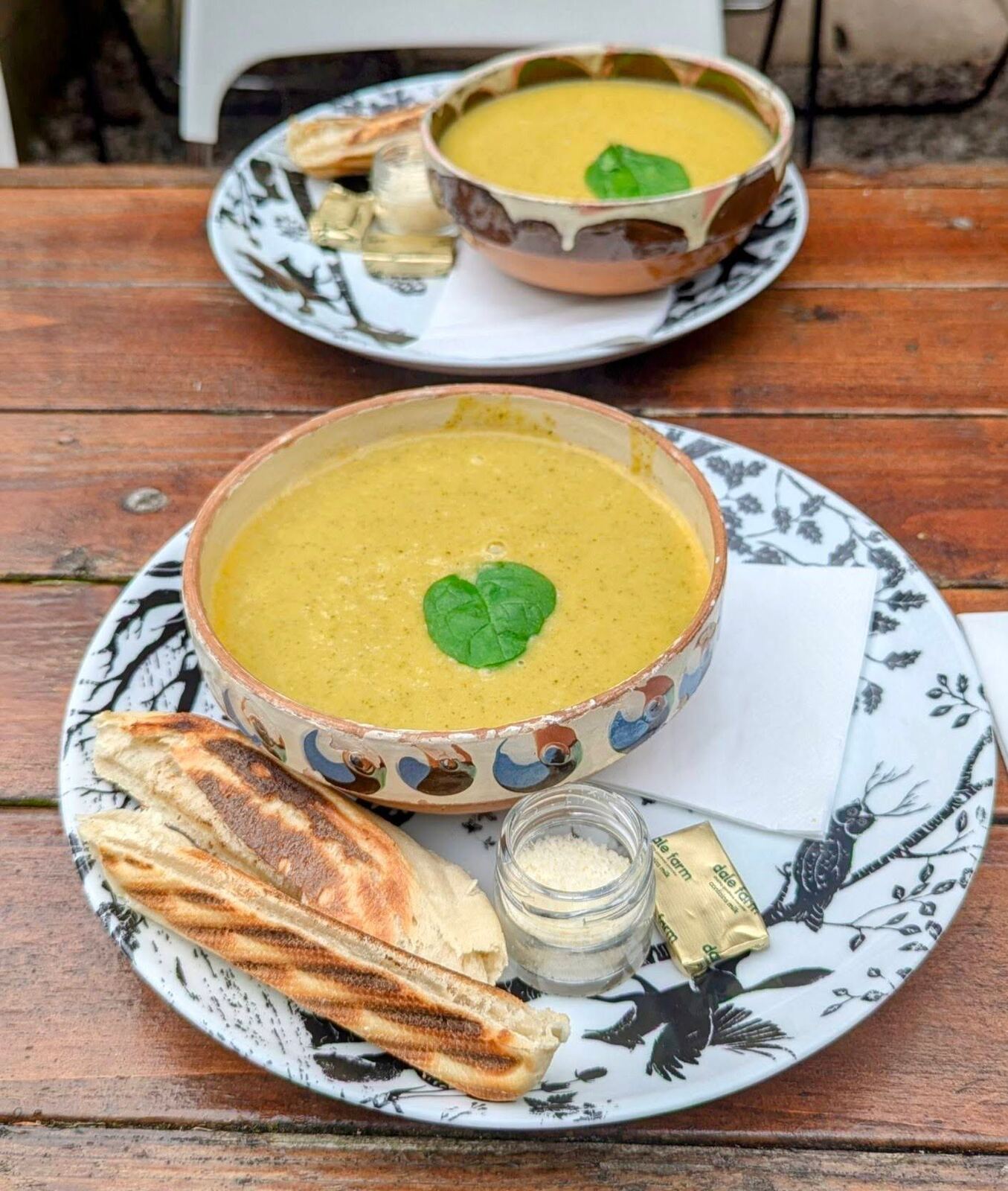 Two bowls of soup with grilled bread and butter on patterned plates on a wooden café table at the Pentland Hills.