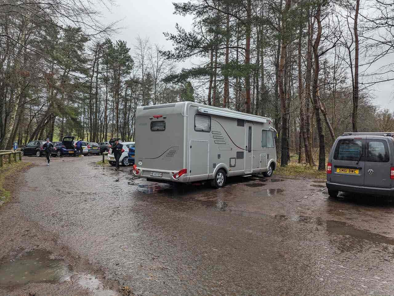 A white Hymer motorhome and a VW T25 campervan parked in the wet Flotterstone car park in the Pentland Hills on a grey winter day.