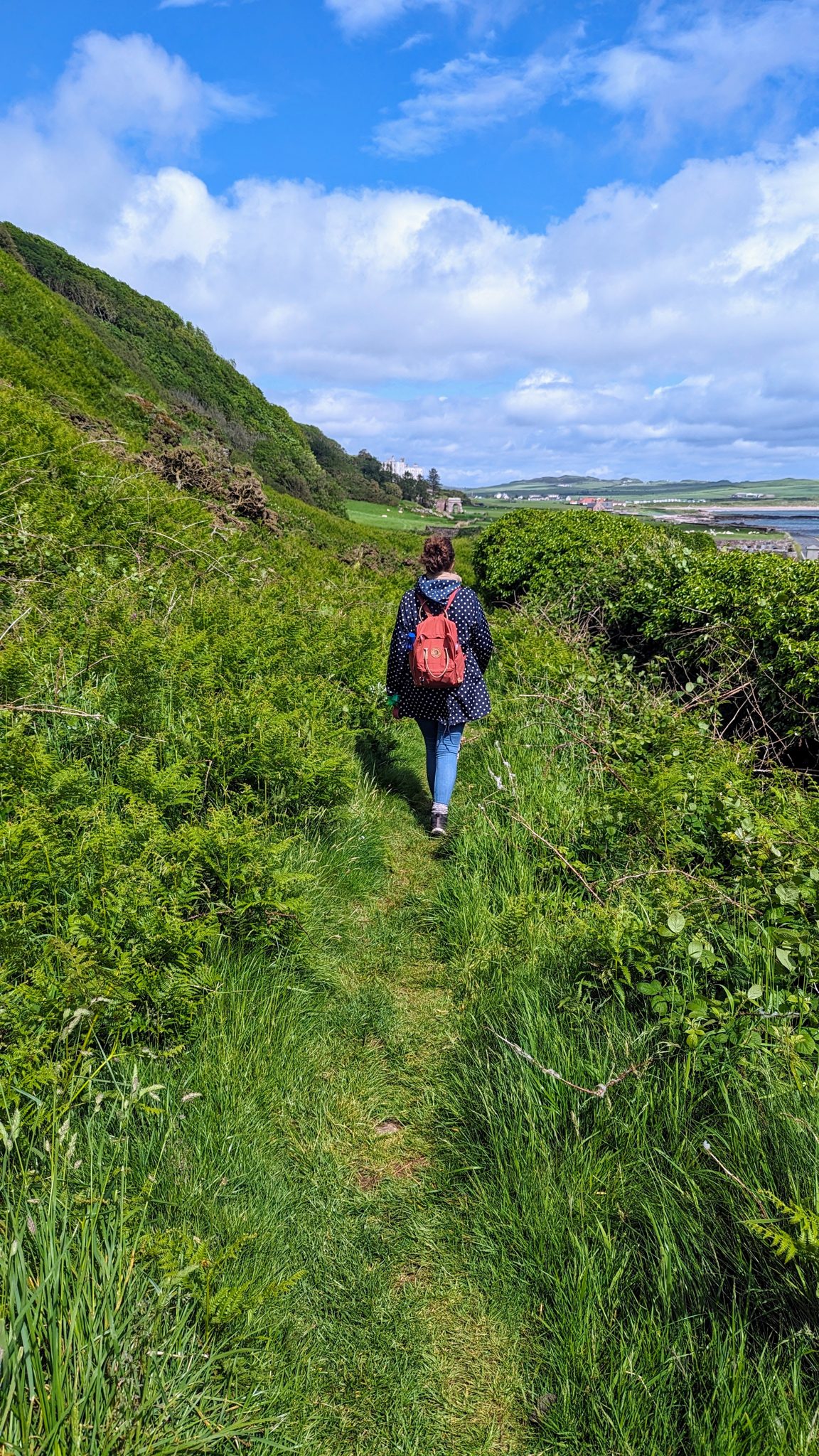 A walker on the green coast path above the sea at Southend, Kintyre.