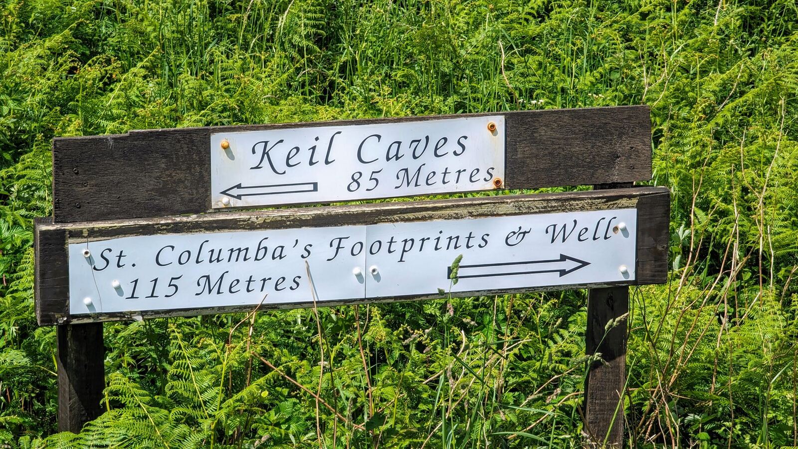 A wooden signpost pointing to Keil Caves and St Columba's Footprints & Well near Southend.