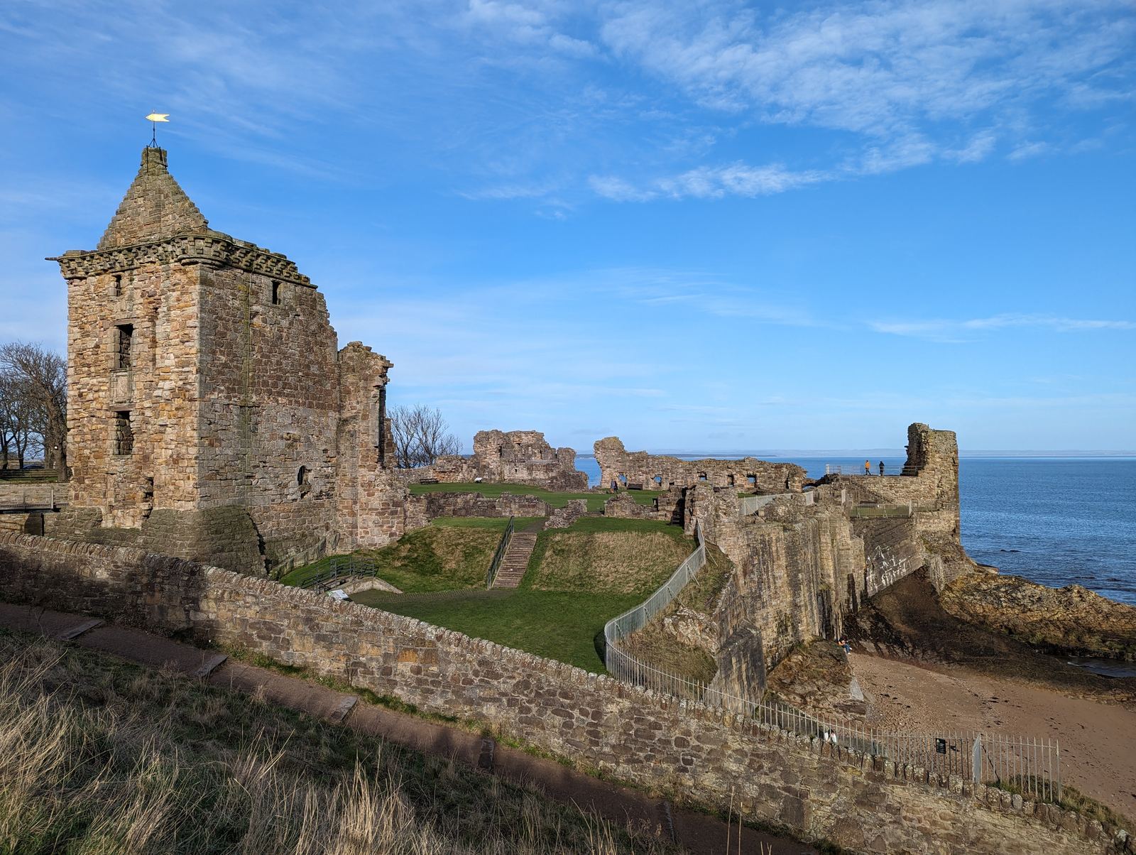 The ruins of St Andrews Castle on the clifftop under a blue sky.