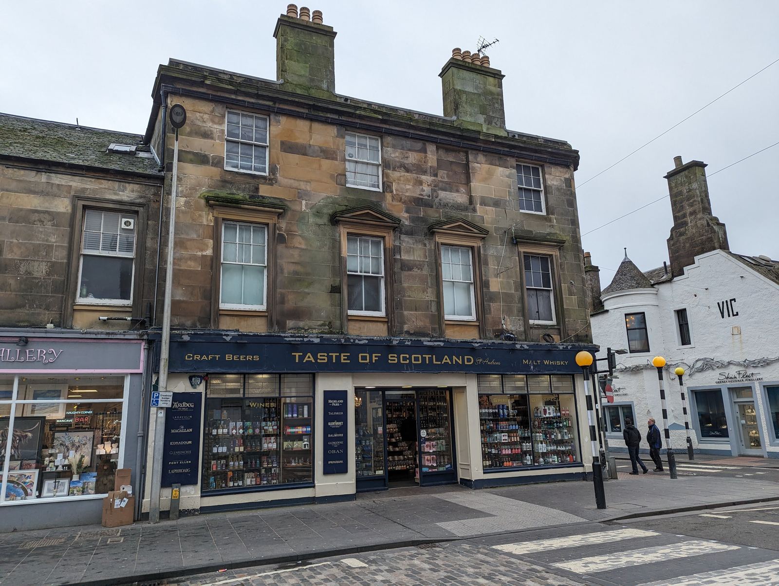 A red sandstone building and shops on a street in St Andrews town centre.