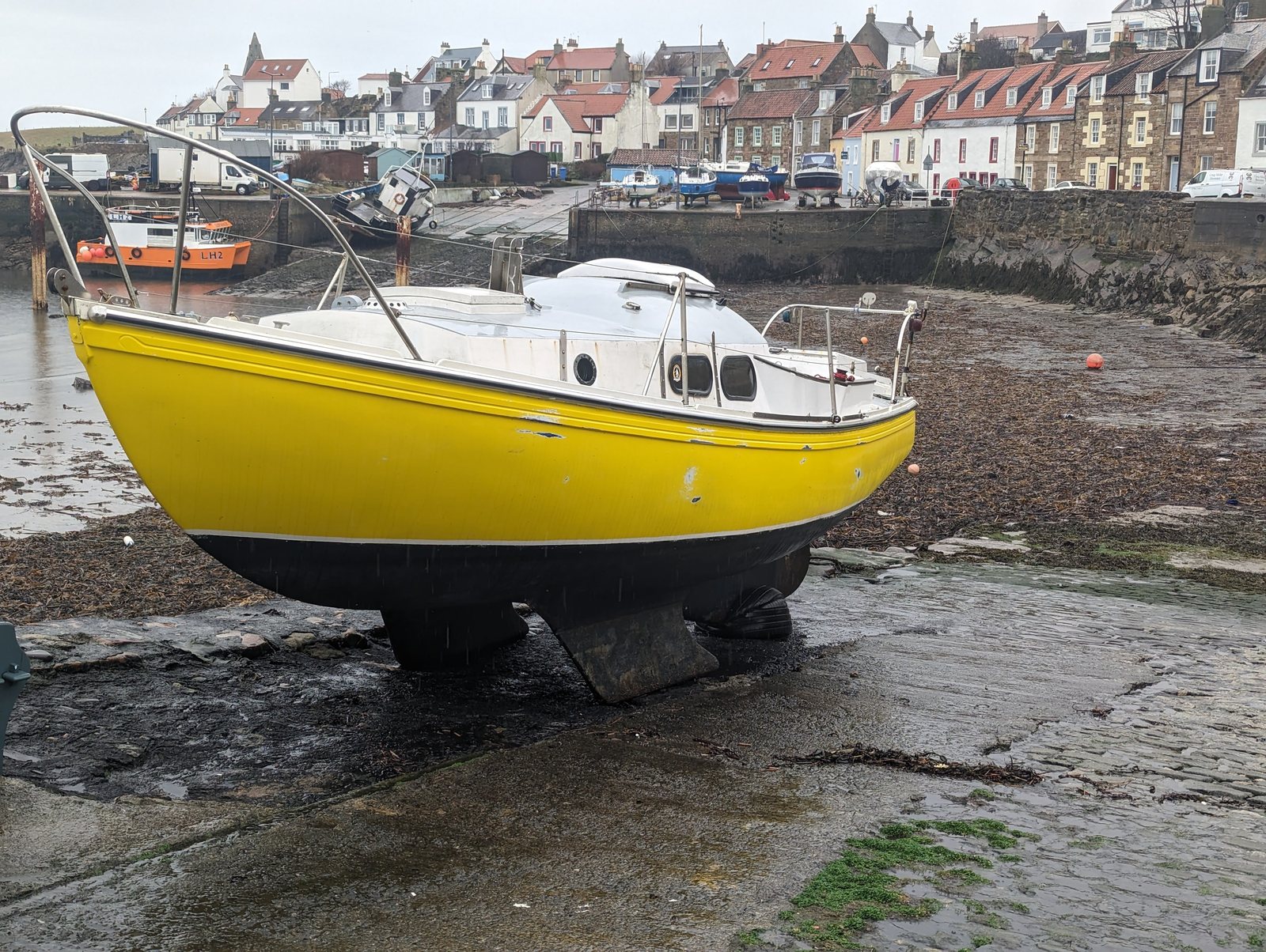 A yellow yacht on the hard at St Monans harbour, the village behind.