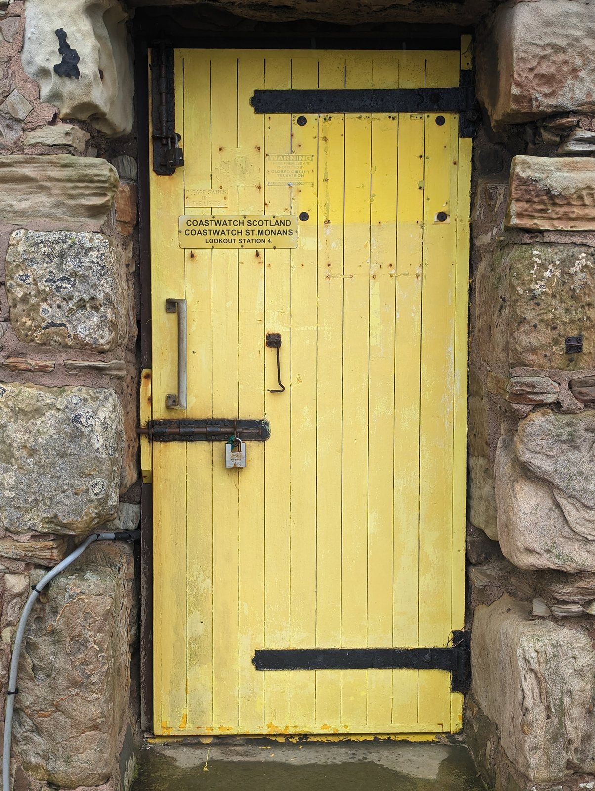 The yellow door of St Monans windmill in its stone wall.