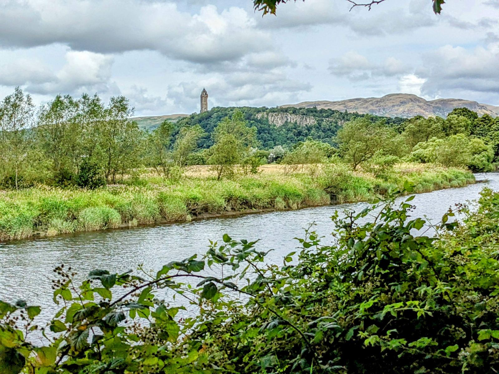 The green grounds and low ruined foundations of Cambuskenneth Abbey by the River Forth, hills beyond.
