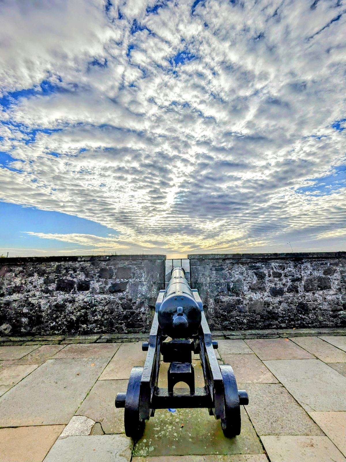 An old cannon on the ramparts of Stirling Castle, the carse and Ochil Hills stretching away beyond under a rippled sky.