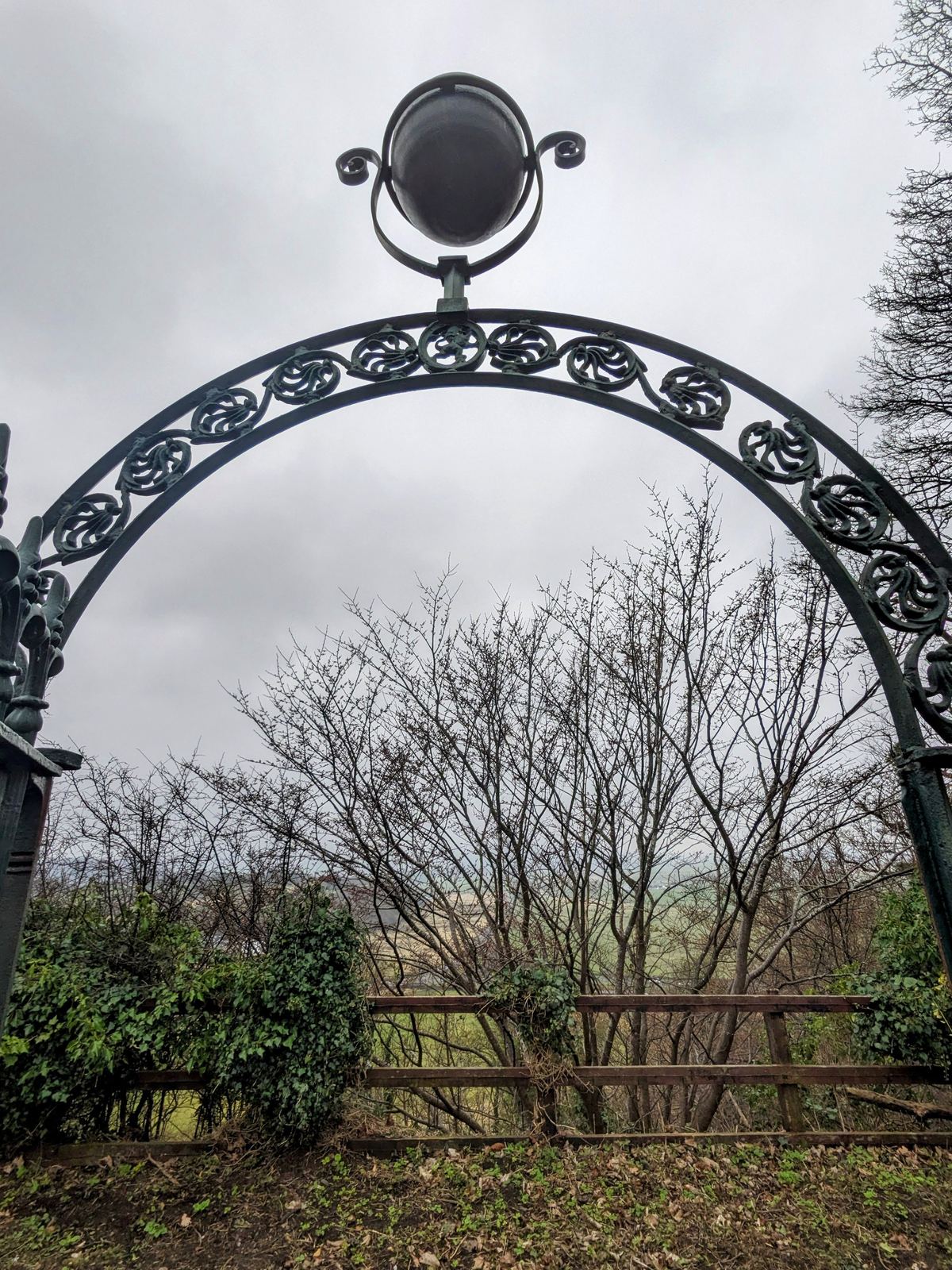 A decorative wrought-iron archway leading into the Old Town Cemetery beneath Stirling Castle.