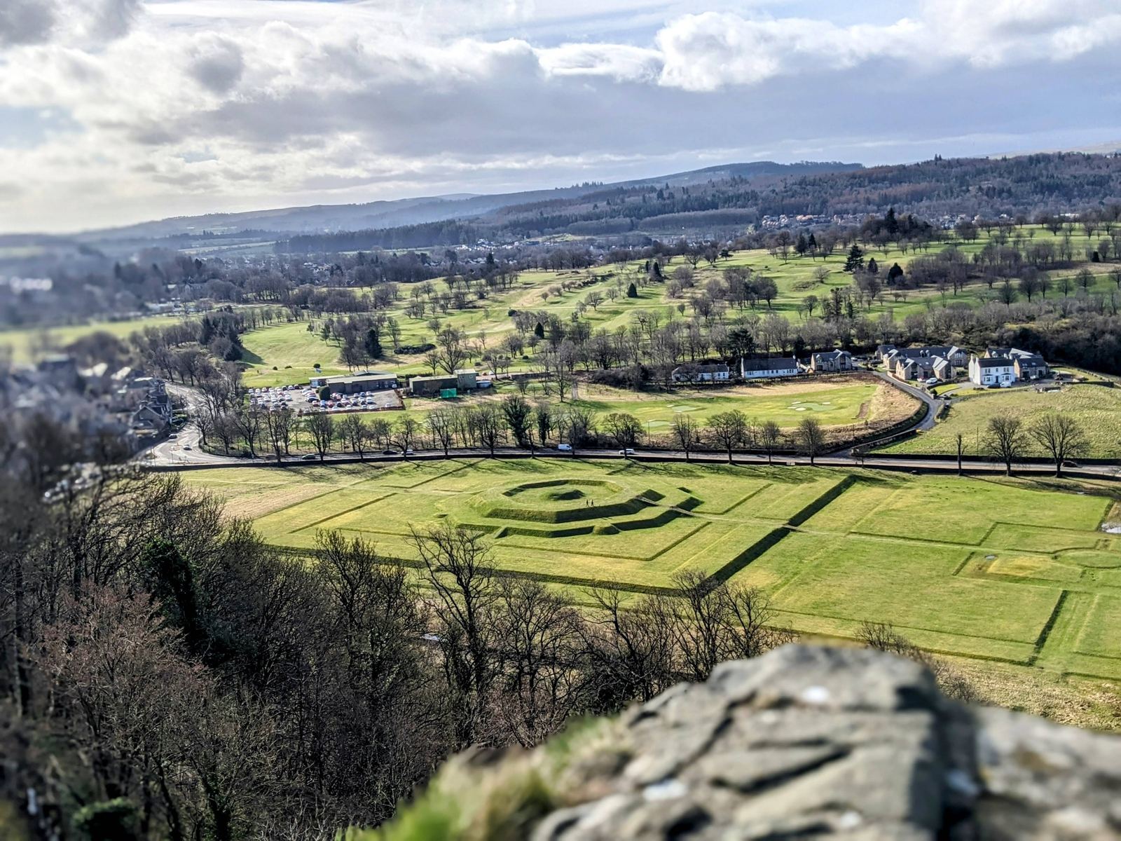 Rows of weathered gravestones on a grassy hillside in Stirling's Old Town Cemetery, a white house and trees beyond.