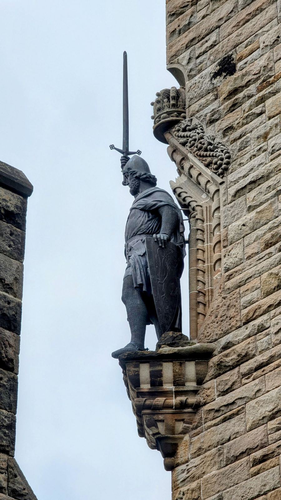 A stone statue of William Wallace in armour, sword in hand, set into the base of the Wallace Monument tower.
