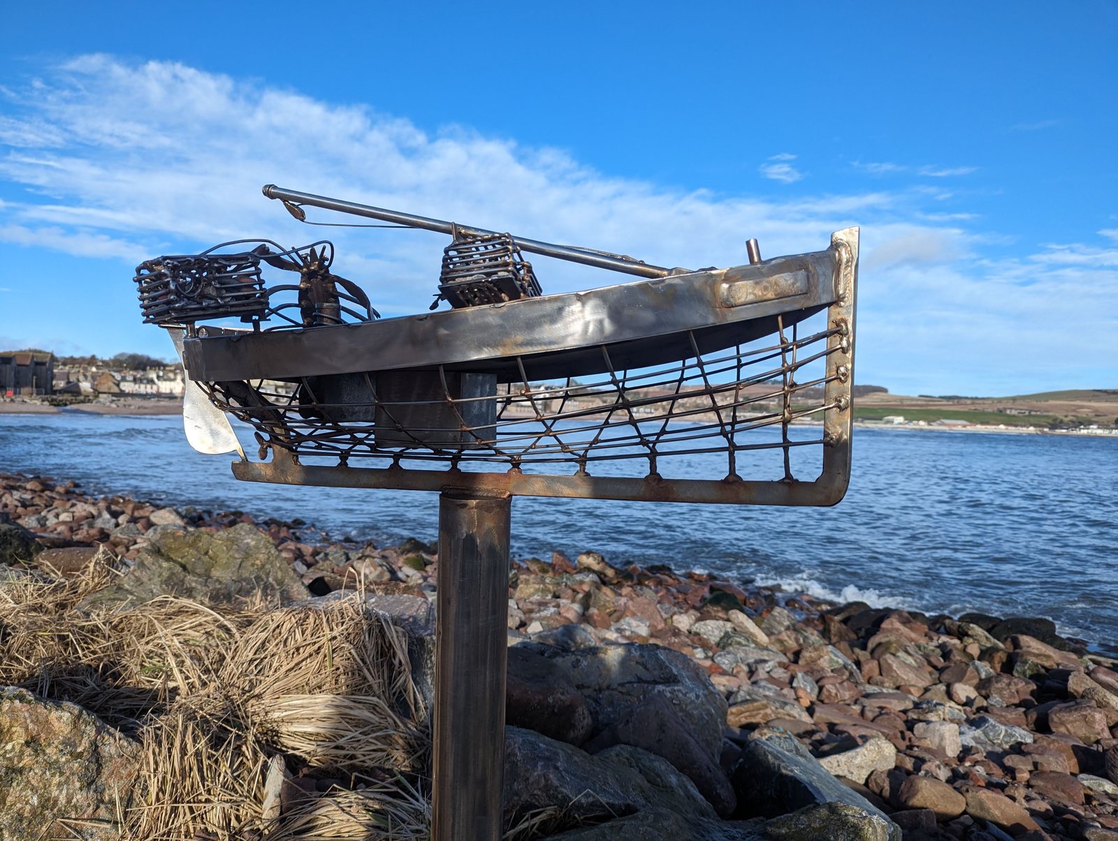 A wire fishing-boat sculpture on the rocks with the sea beyond, Stonehaven.