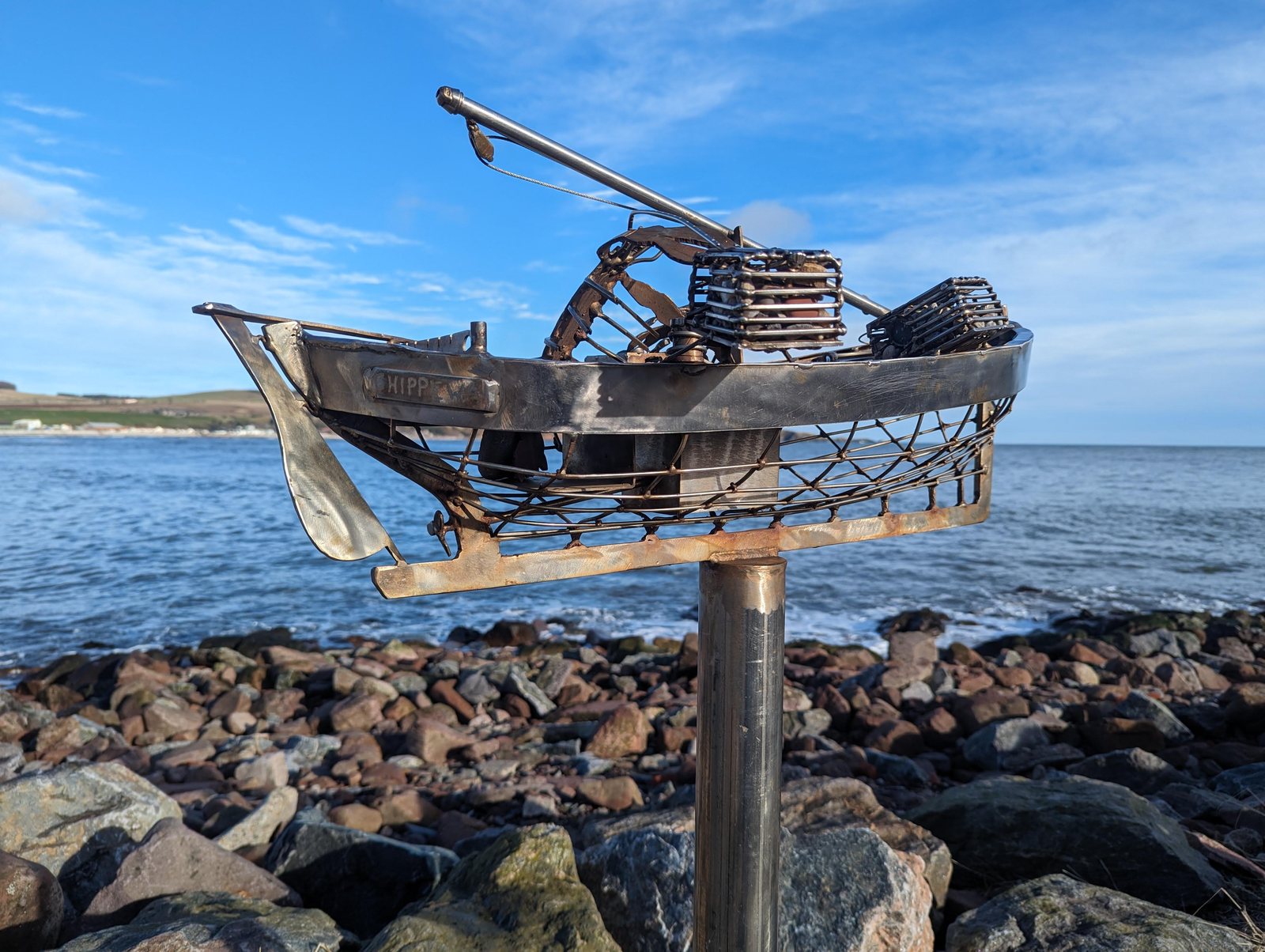 A metal sculpture of a fishing boat piled with creels on the shore at Stonehaven.