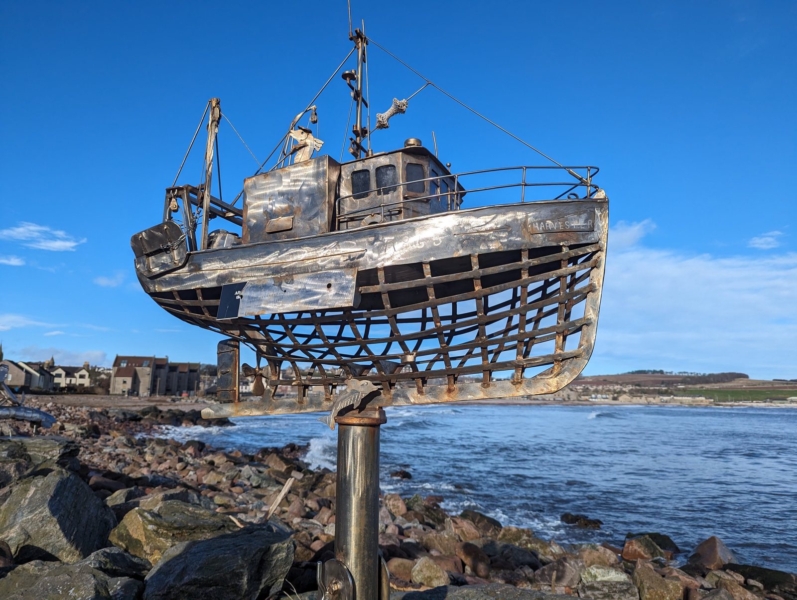 A metal fishing-boat sculpture perched on a post above the rocks, Stonehaven.