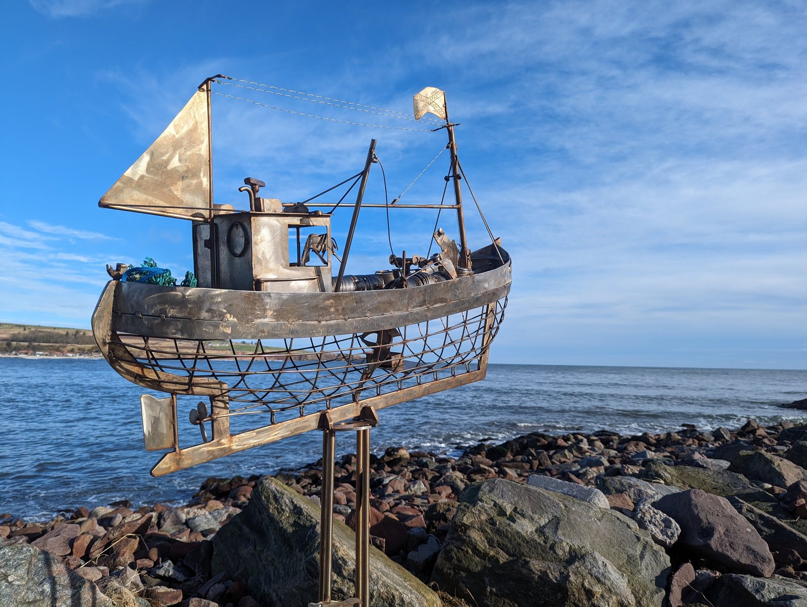A detailed metal fishing-boat sculpture on the shoreline rocks, Stonehaven.
