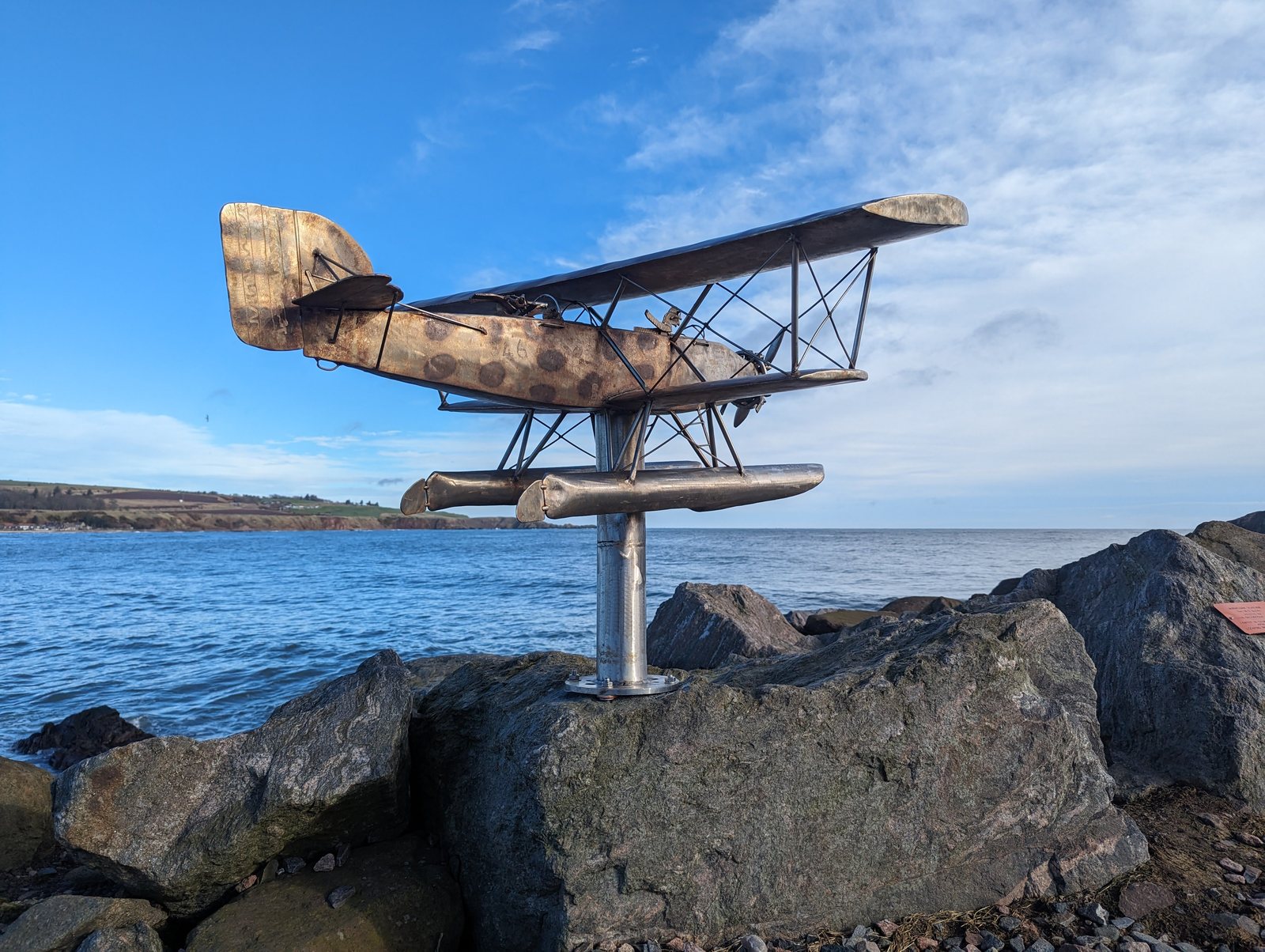A metal flying-boat sculpture on a post above the rocks, Stonehaven.