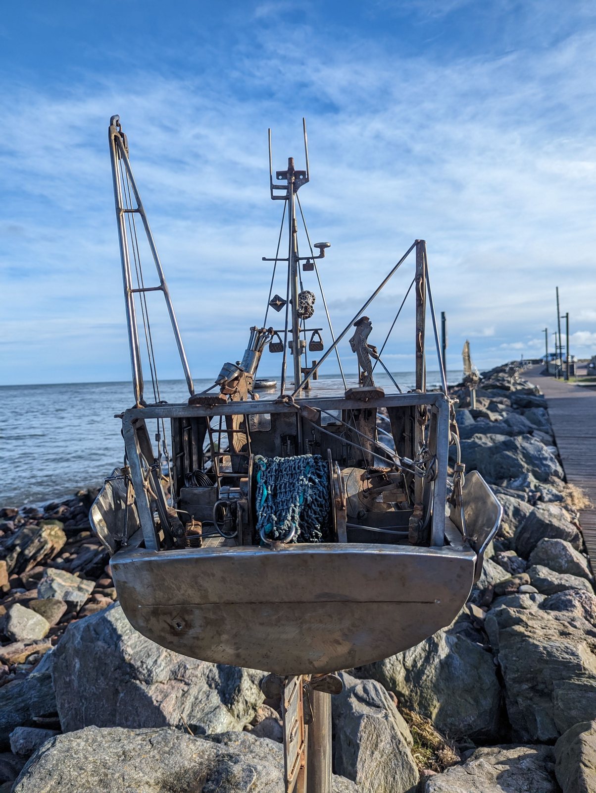 A trawler sculpture with a metal font in the foreground on the Stonehaven shore.