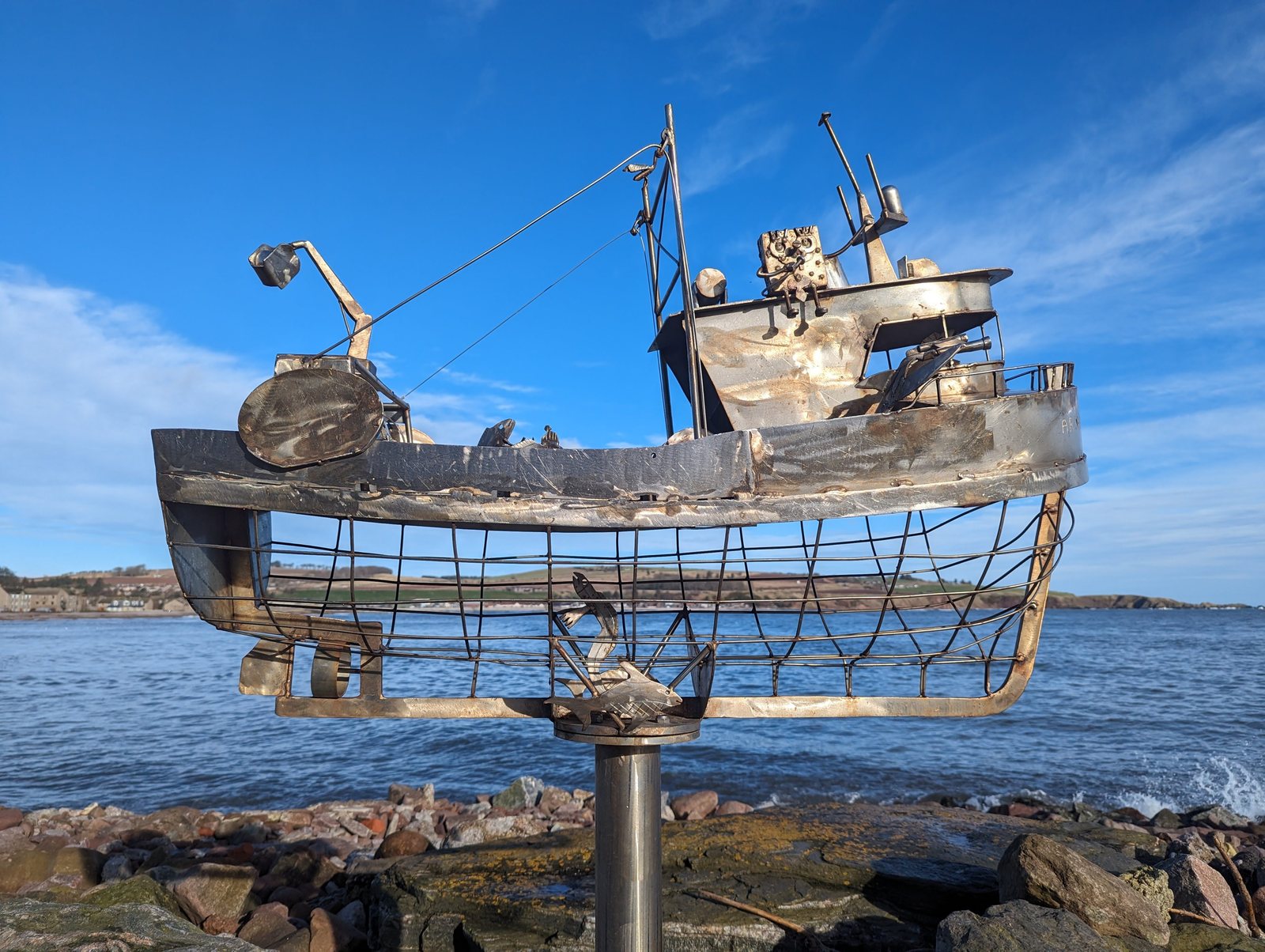 A metal trawler sculpture rigged with gantries on the Stonehaven shore.