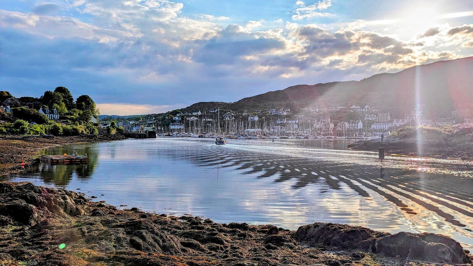 A golden sunset reflected in the calm water of Tarbert harbour, sun-rays across the loch.